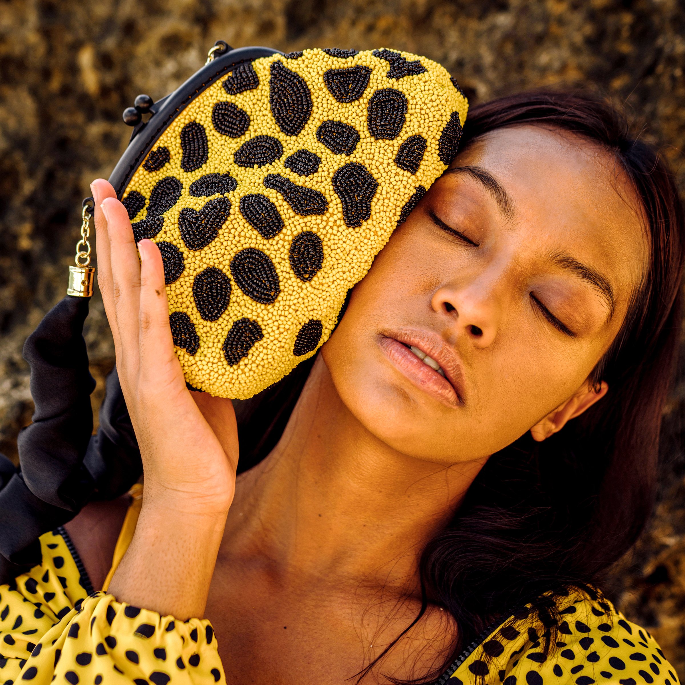 ARNOLDI VENOM Hand-beaded Clutch Bag featuring intricate black and yellow glass bead patterns, soft satin scrunch handle, and elegant design.