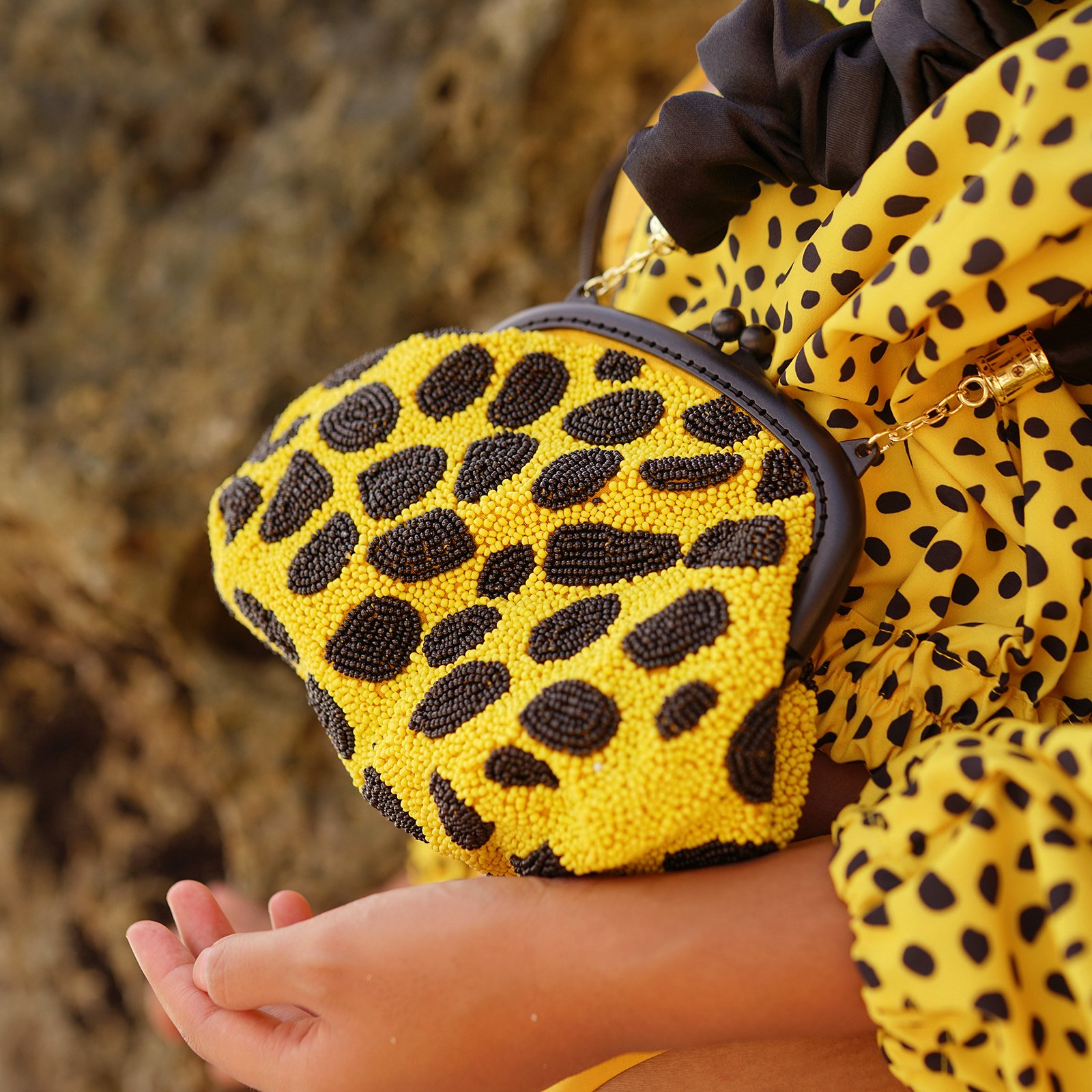 ARNOLDI VENOM Hand-beaded Clutch Bag featuring intricate black and yellow glass bead patterns, soft satin scrunch handle, and elegant design.