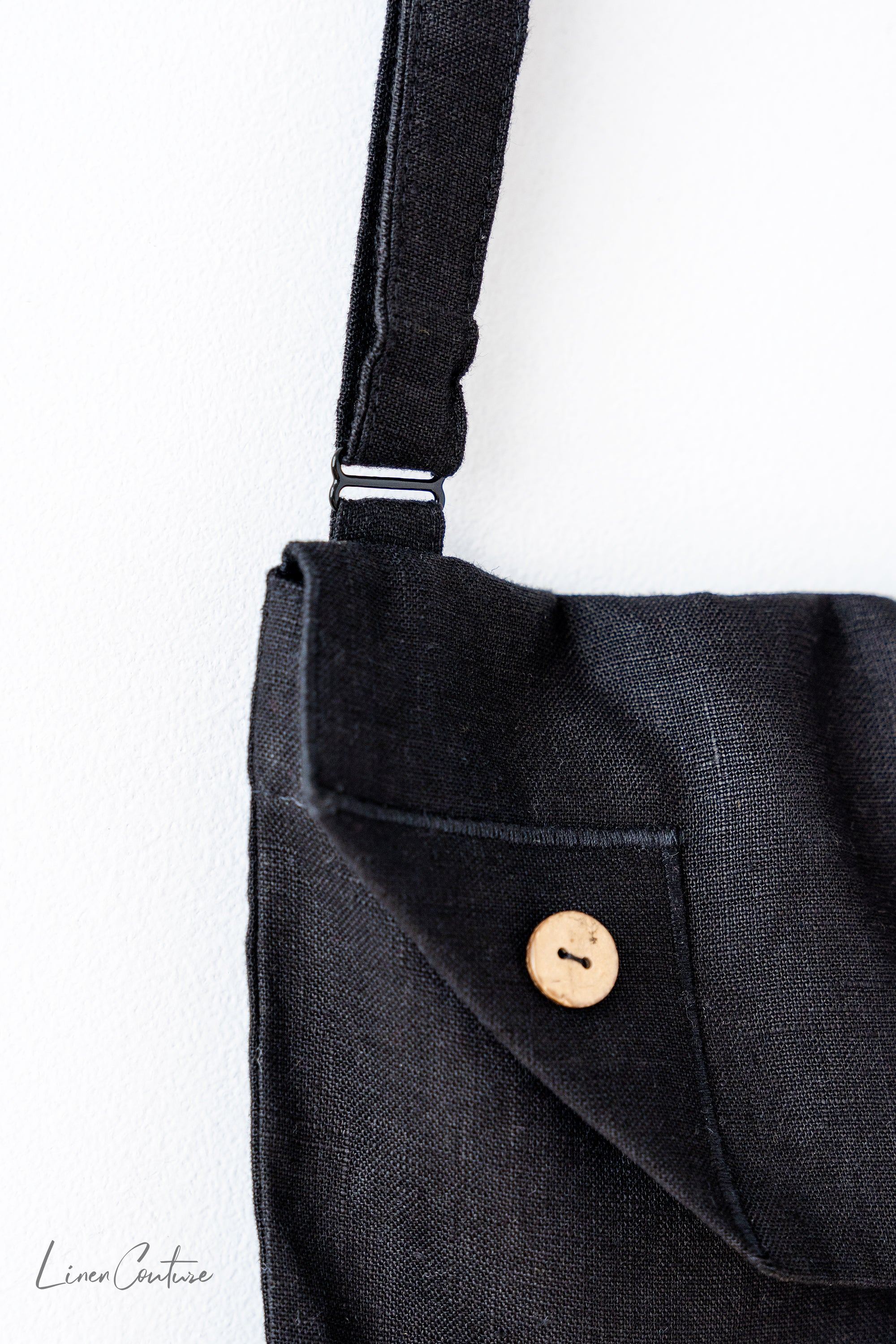 Black linen shoulder bag featuring coconut buttons and an adjustable strap, showcasing its elegant design and quality craftsmanship.