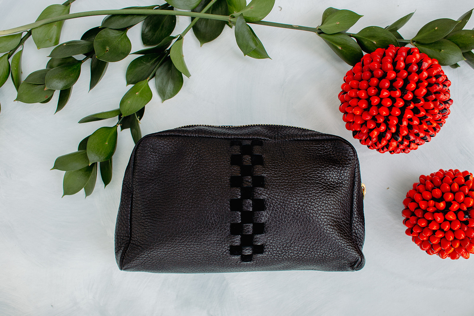 A stylish leather woven makeup case in black with gold plated hardware, featuring a vibrant cotton lining and a convenient zipper design.