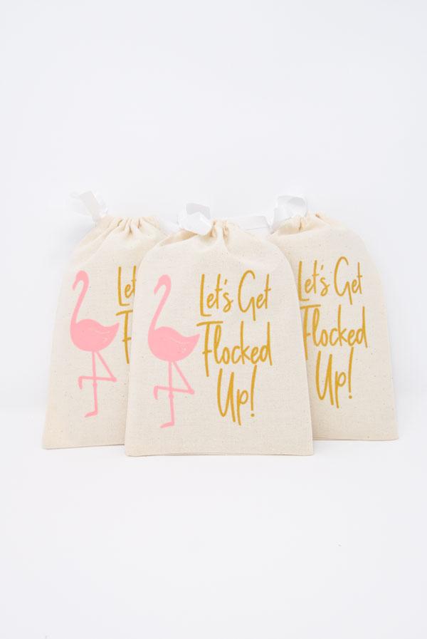 A vibrant canvas bag featuring a pink flamingo and glittery gold text that says 'Let's Get Flocked Up', perfect for hangover kits and party favors.