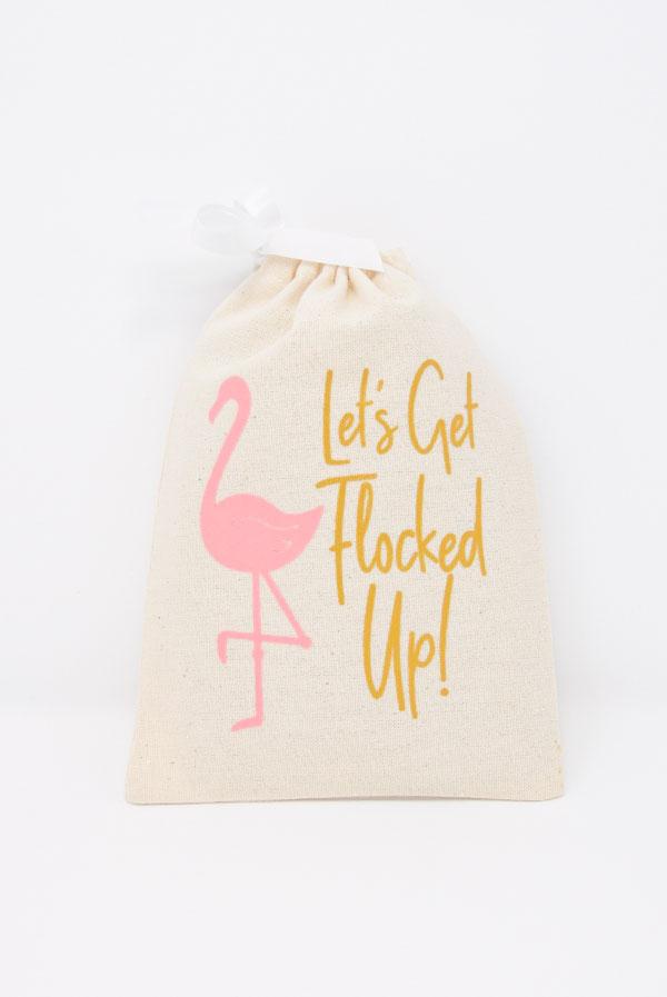 A vibrant canvas bag featuring a pink flamingo and glittery gold text that says 'Let's Get Flocked Up', perfect for hangover kits and party favors.