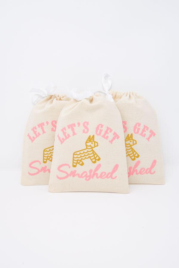 Colorful Let's Get Smashed! Fiesta Hangover Kit Bag featuring a glittery gold piñata design and pink text, perfect for party favors.