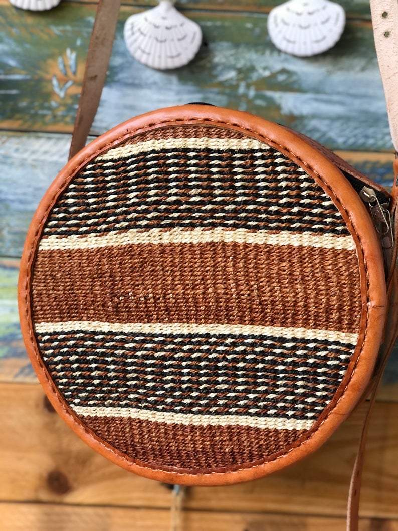 A beautifully handwoven African Round Sisal Sling Bag in brown, showcasing its unique round shape and natural fiber texture.