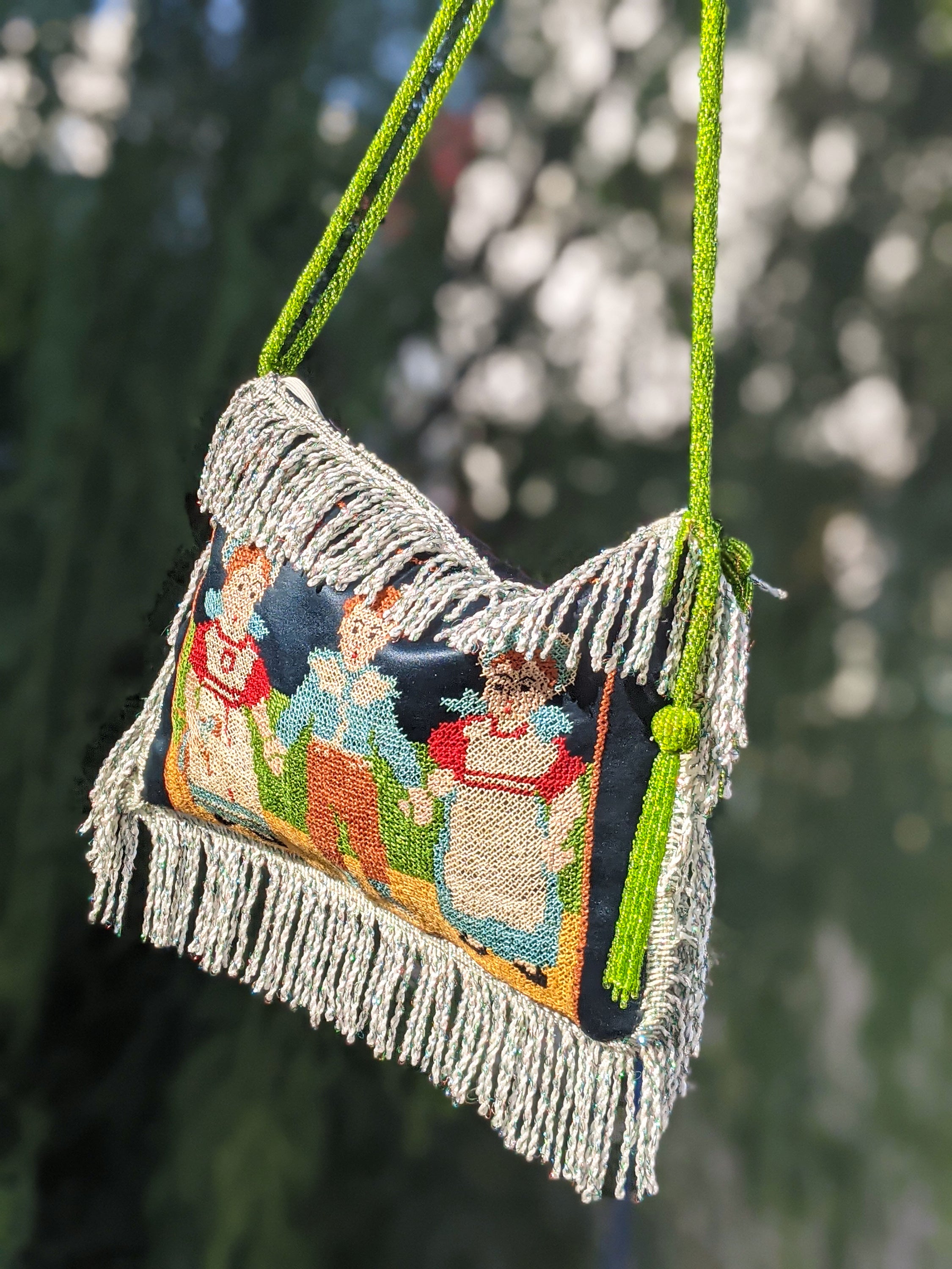 Antique garment cloth bag featuring hand-embroidered peasant figures and green beaded cord handles, showcasing intricate craftsmanship.