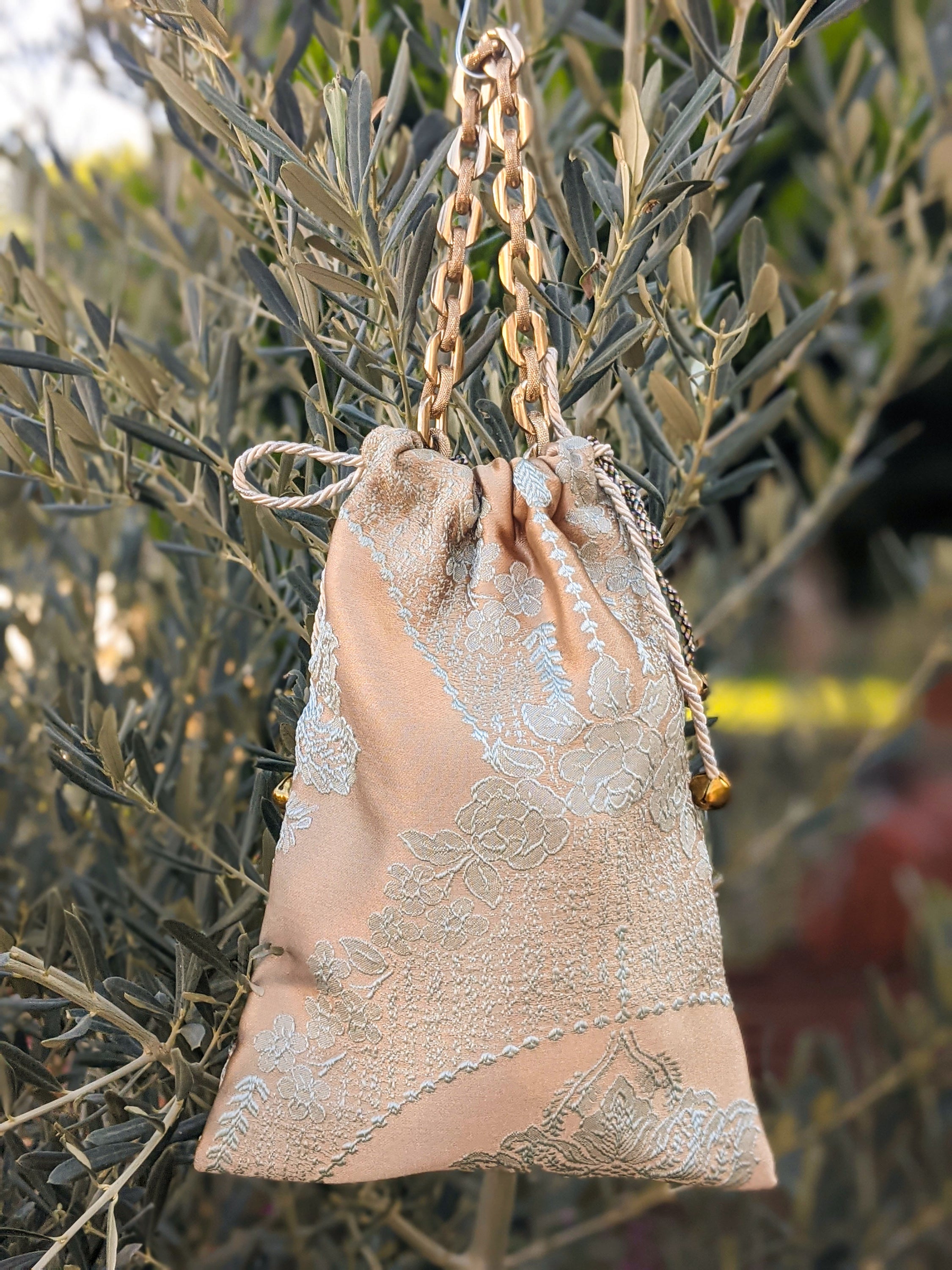 Brown sateen pouch shoulder bag featuring a golden chain handle and shiny grey and cream strings.