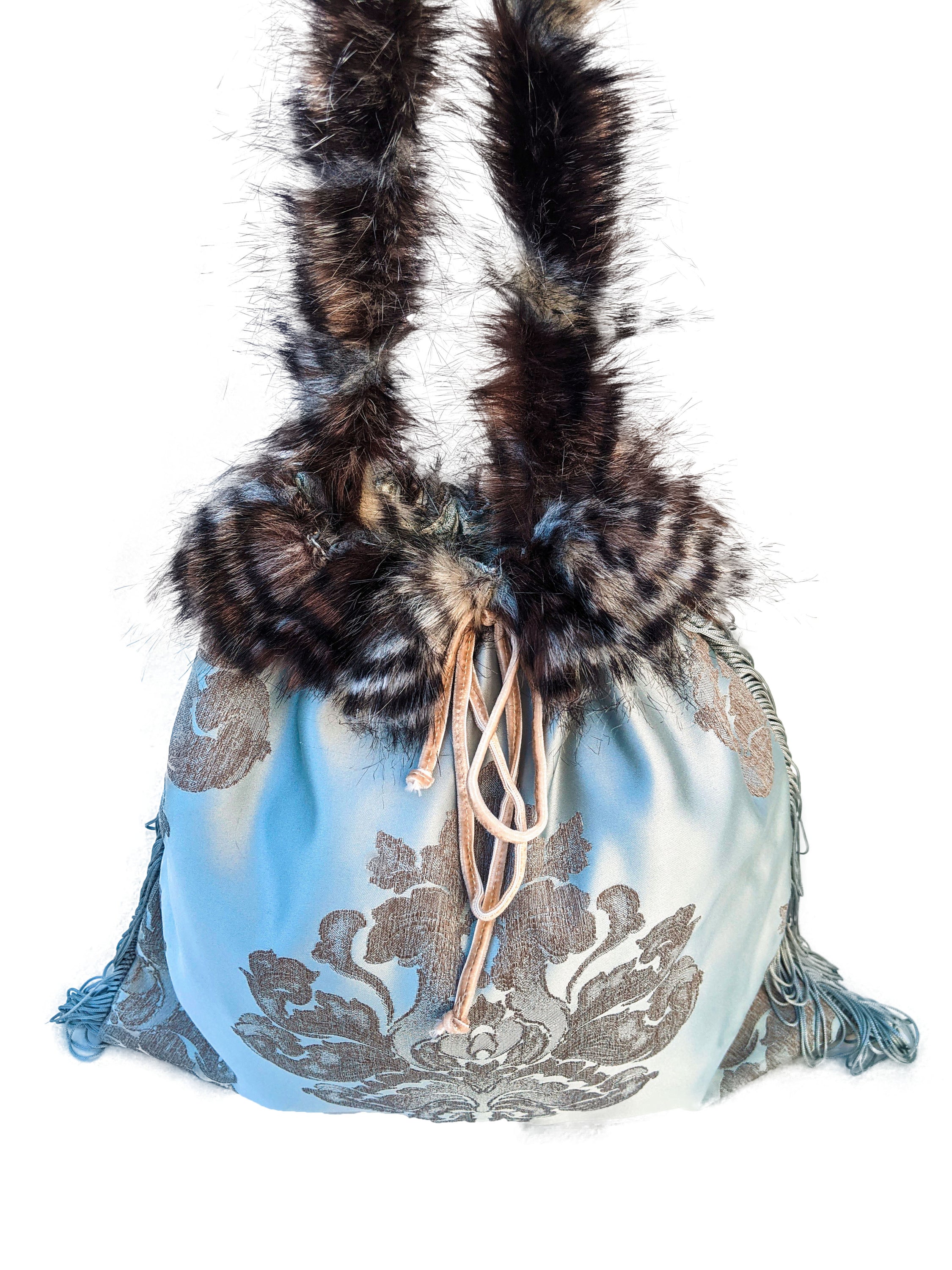 Dendritic Jasper pouch bag featuring silvery blue sateen, faux fur handle, grey fringes, and cream velvet string closure.