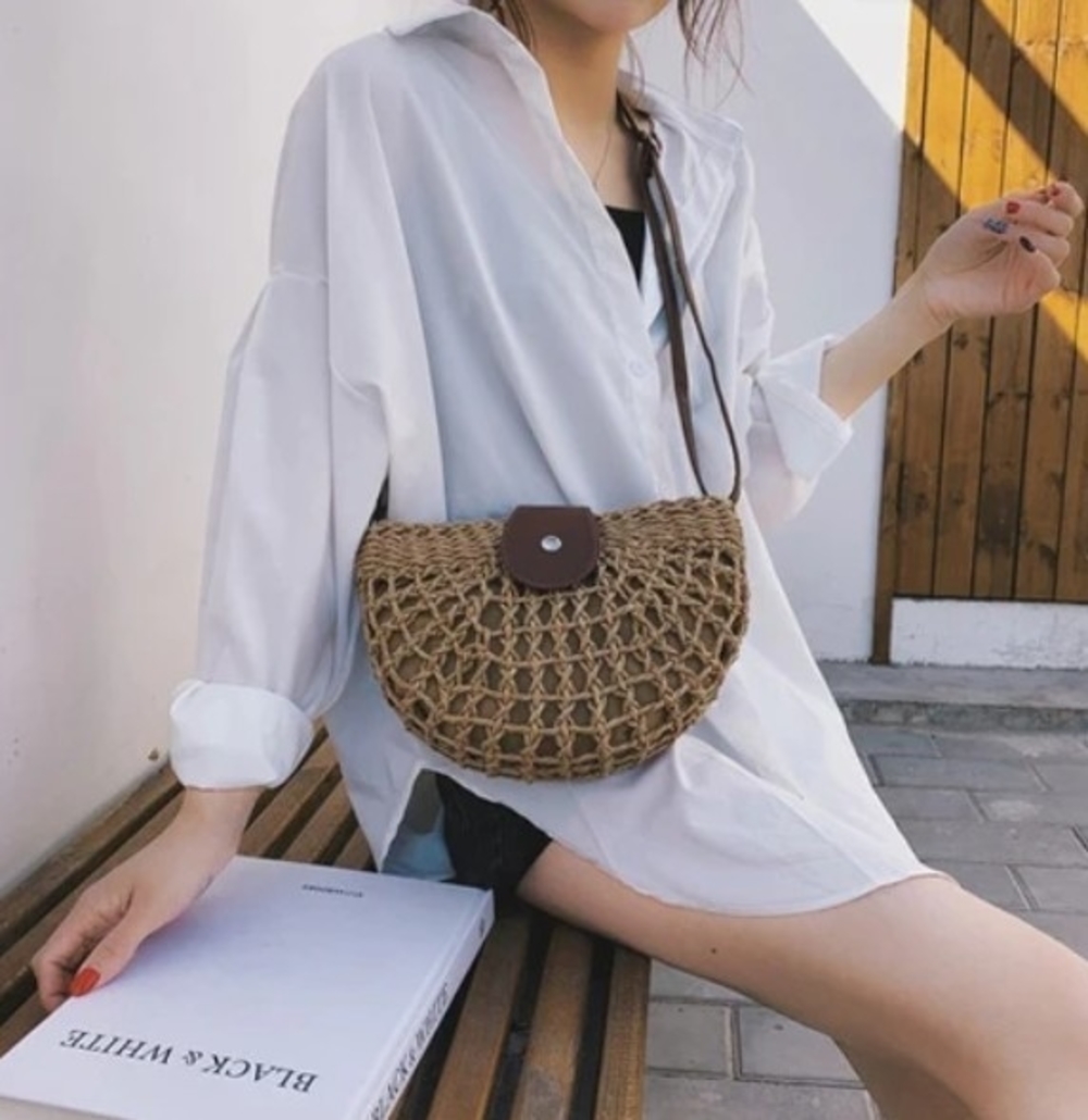 Half Moon Straw Crossbody Bag made of wicker straw with a vegan leather strap, featuring a trendy semi-circle design in brown color.