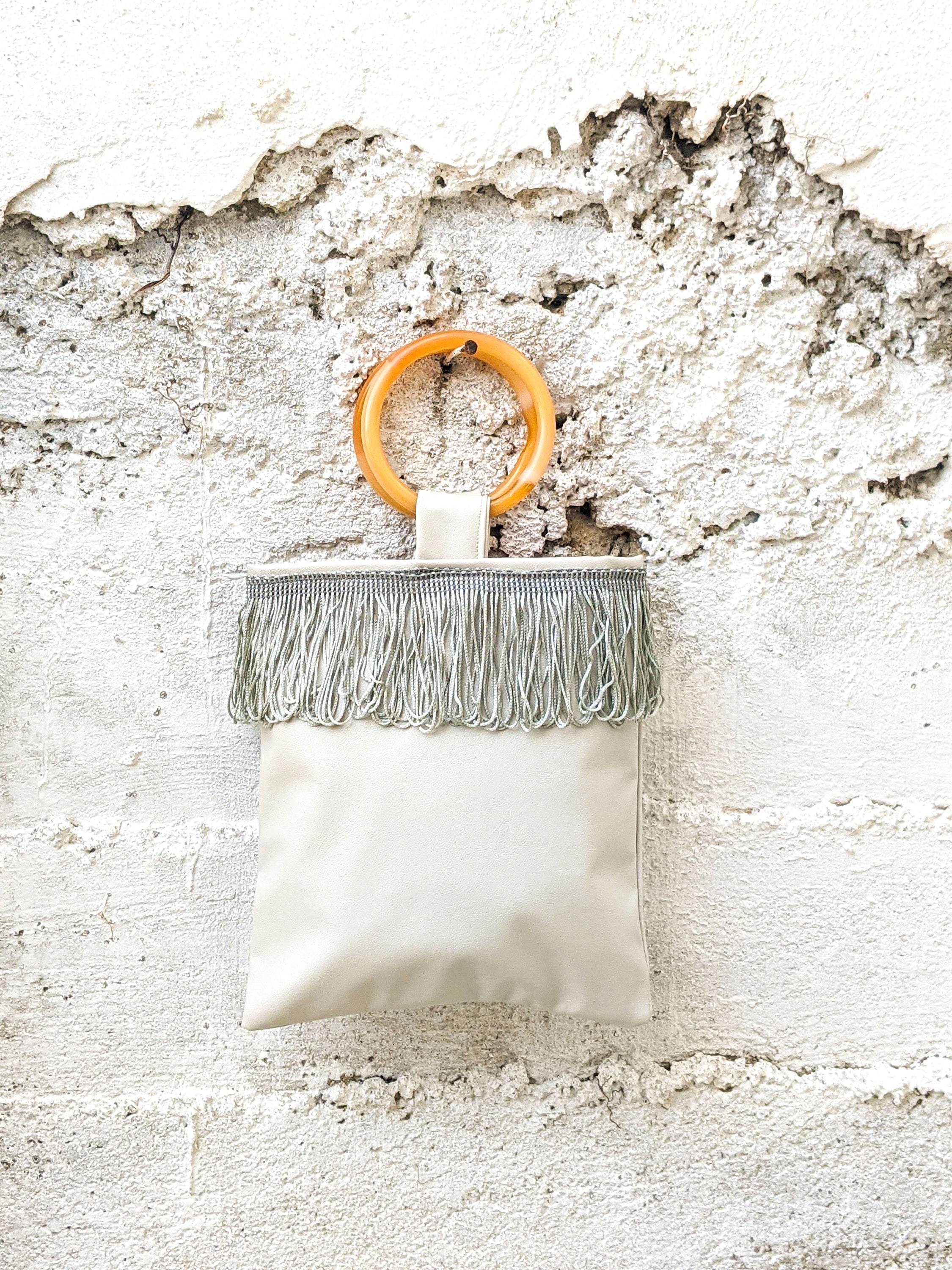 Light grey mini faux leather bag with amber resin handles and grey fringes, showcasing a stylish and compact design.