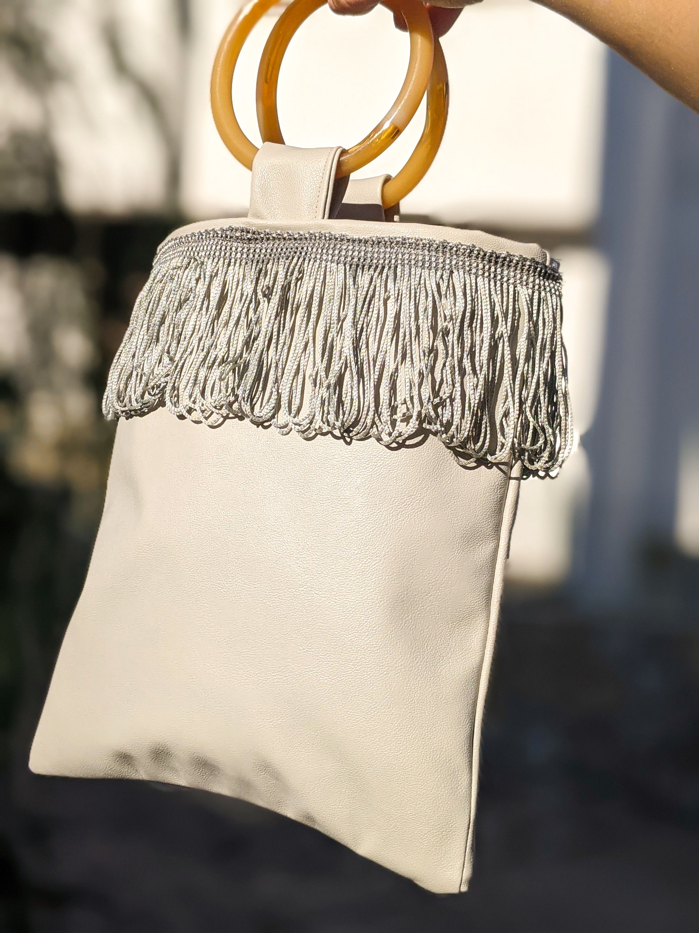 Light grey mini faux leather bag with amber resin handles and grey fringes, showcasing a stylish and compact design.