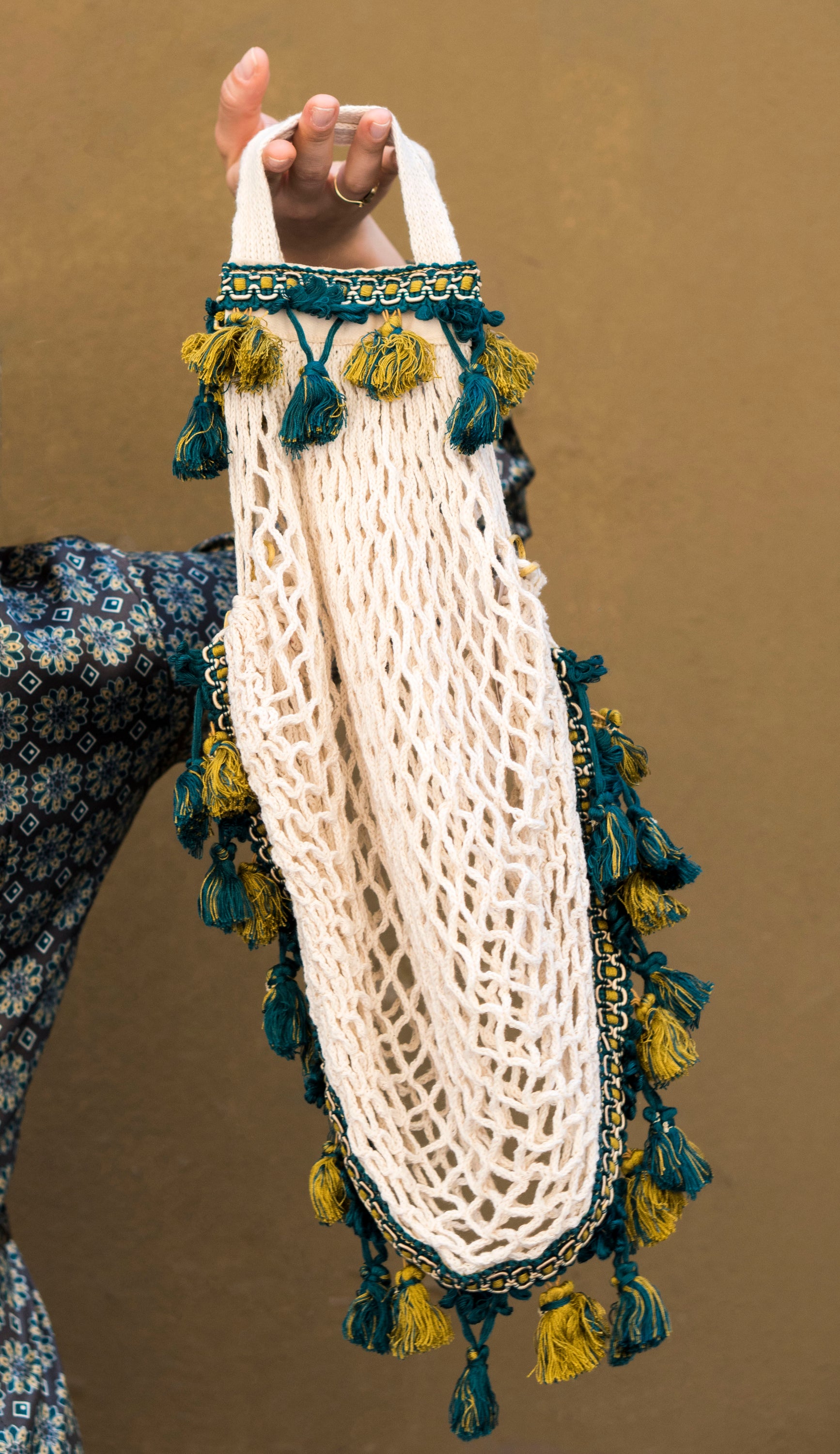 Handmade cotton string bag in natural cream color with yellow-blue tassels and cotton handle.