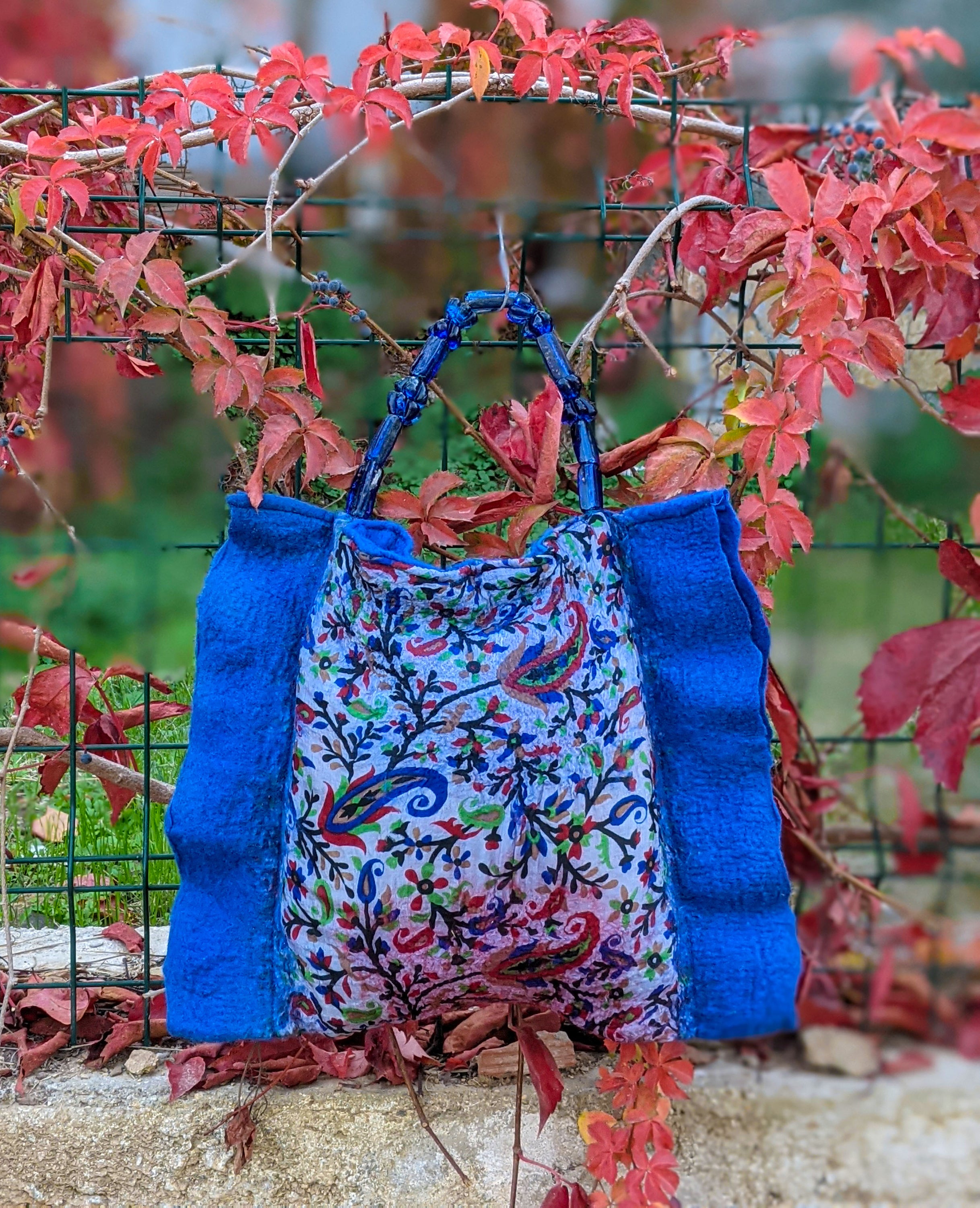 Handmade cobalt blue felt bag with glass bead handle and linen lining, featuring a snap fastener closure.