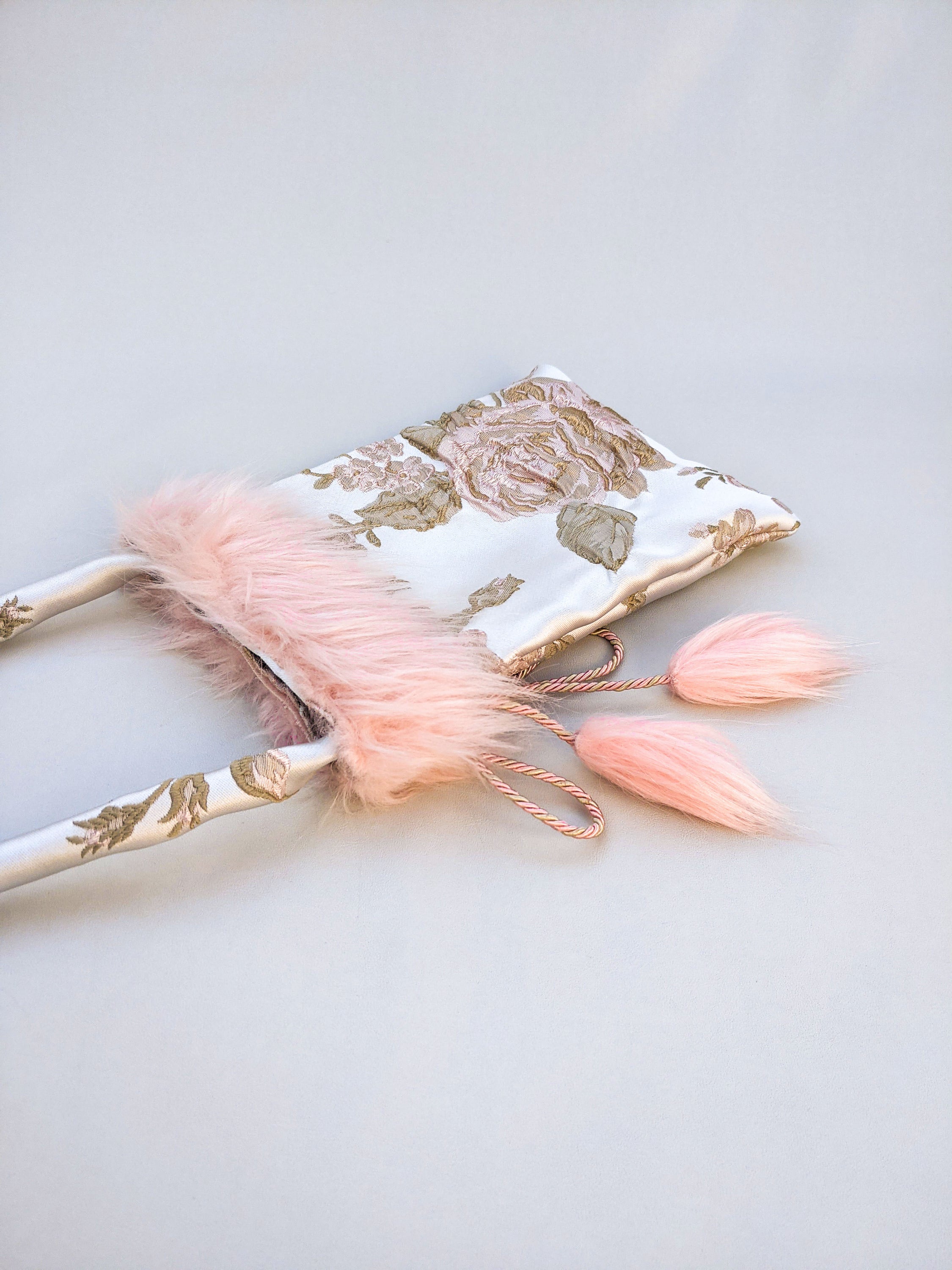 Poppyseed Jasper pouch bag featuring jacquard fabric, pink faux fur details, and a gold-rose cord closure, measuring 17 cm x 26 cm.