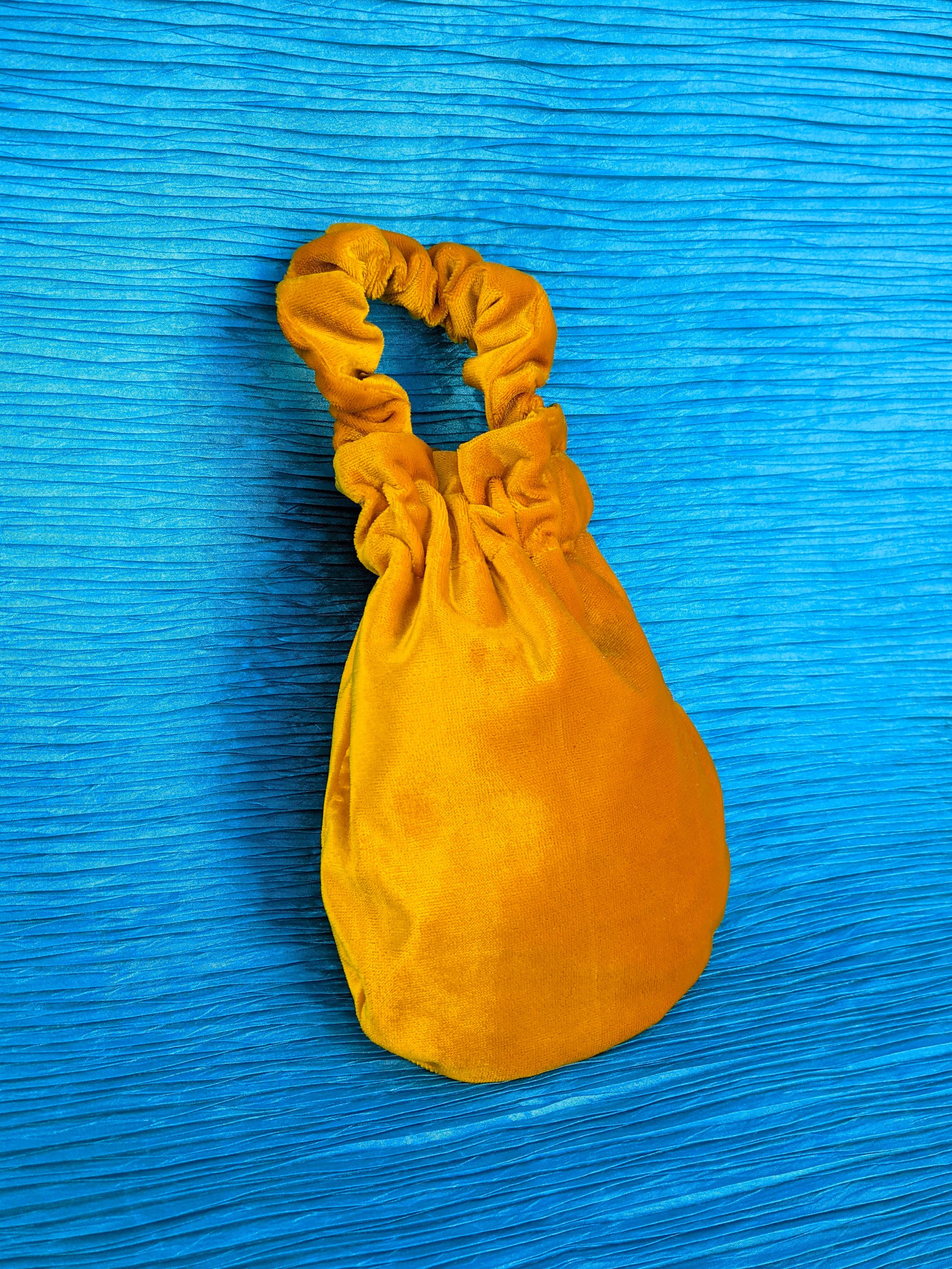 A stylish deep yellow velvet wristlet bag with a sleek design, perfect for various occasions.