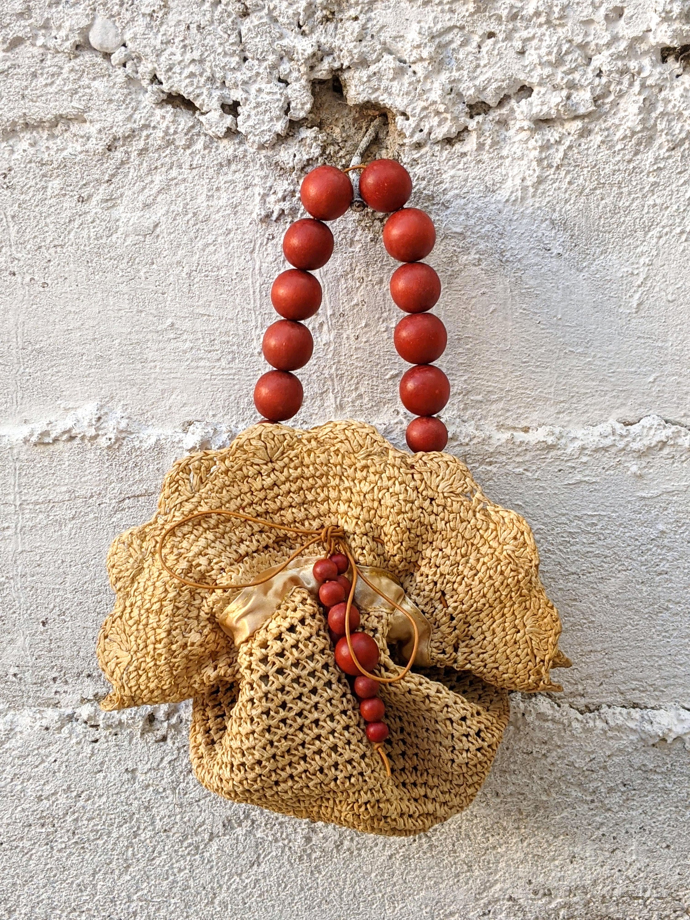 Upcycled straw pouch bag featuring a drawstring closure, wooden bead handle, and snap fastener, showcasing eco-friendly fashion.