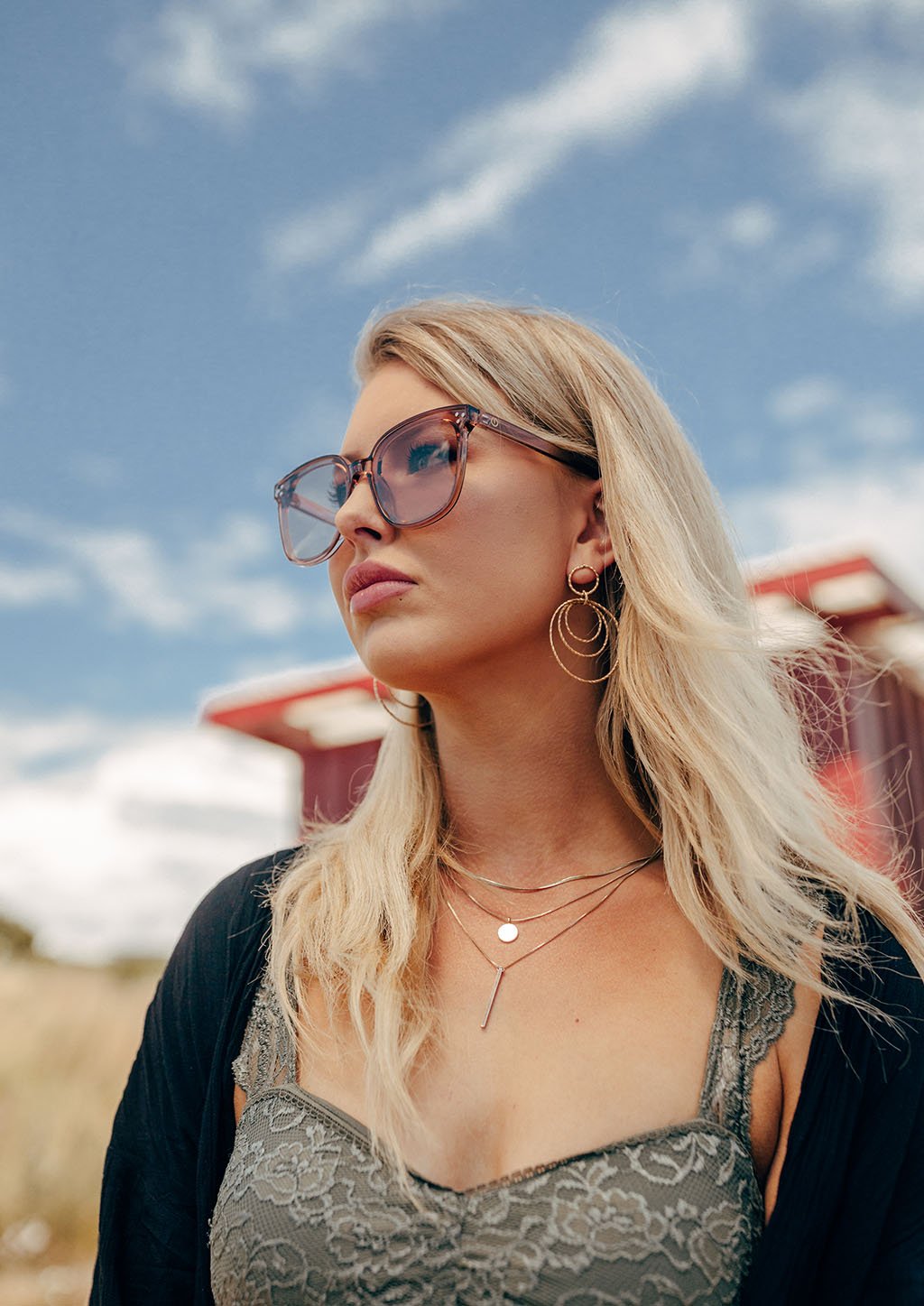 A pair of Jasmine sunglasses from the Babylon Series featuring a classic wayfarer shape and vibrant colors, set against a rustic wooden background.