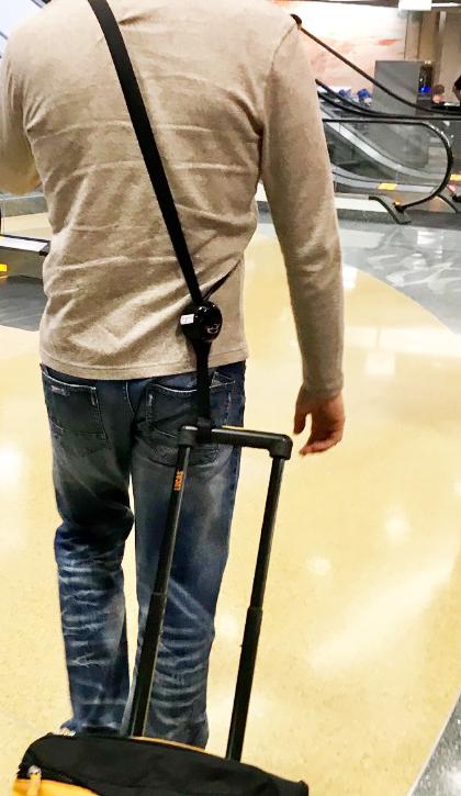 RetraStrap hands-free luggage strap attached to a wheeled carry-on, showcasing its ergonomic design and anti-theft features.