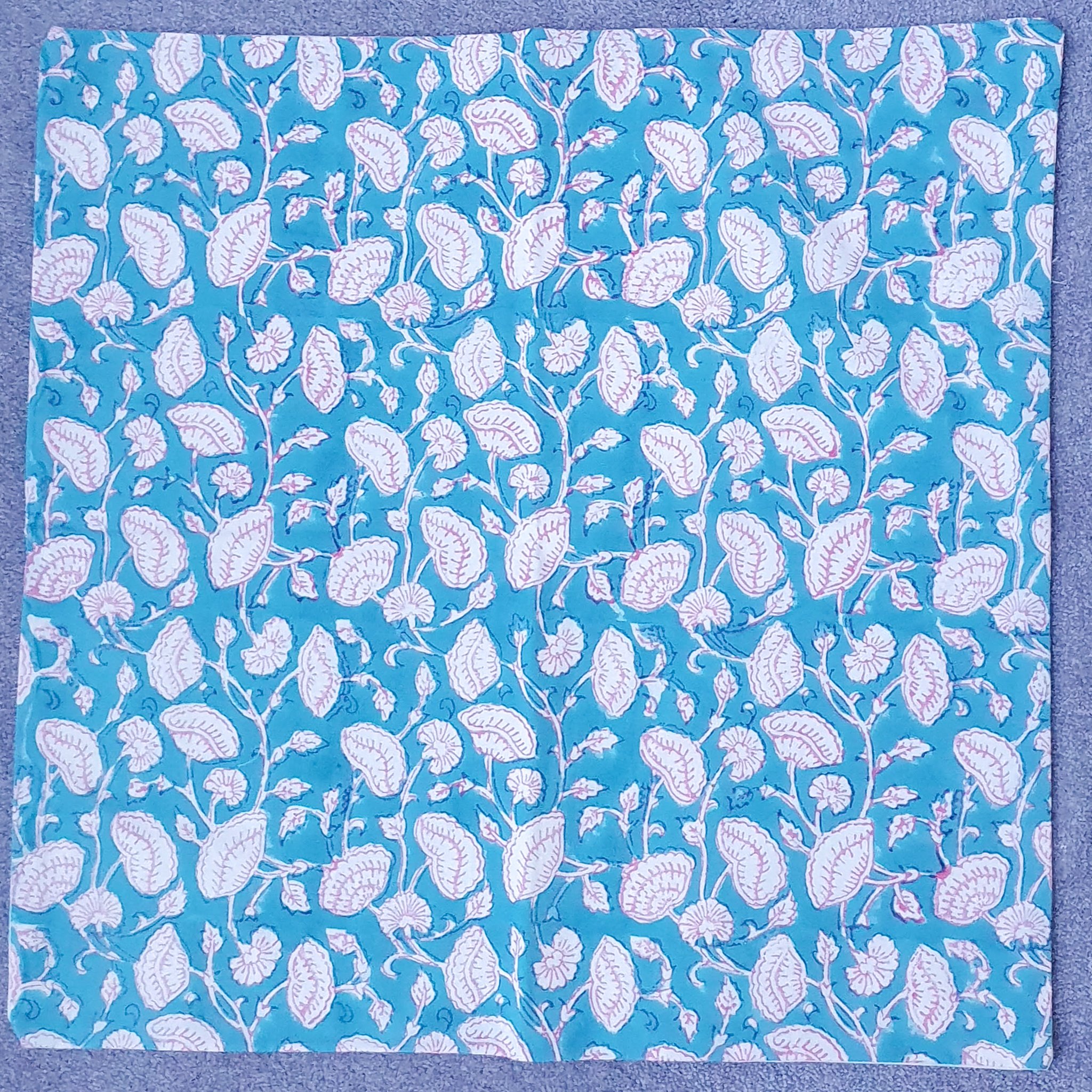 Handmade block-printed cushion cover featuring floral patterns in teal with pink outline, showcasing artisan craftsmanship.