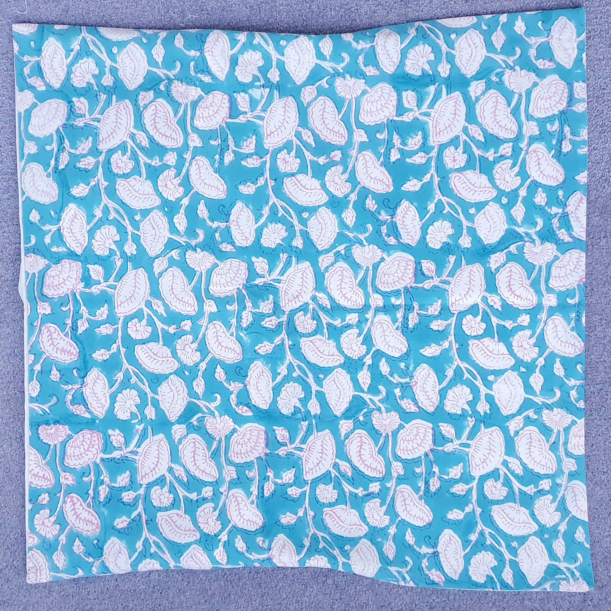 Handmade block-printed cushion cover featuring floral patterns in teal with pink outline, showcasing artisan craftsmanship.