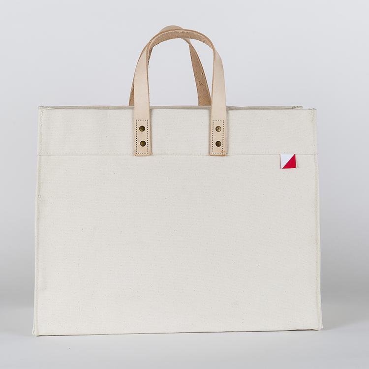 A stylish Box Tote Bag made of heavyweight canvas with thick leather handles and metal studs, perfect for outdoor gatherings.