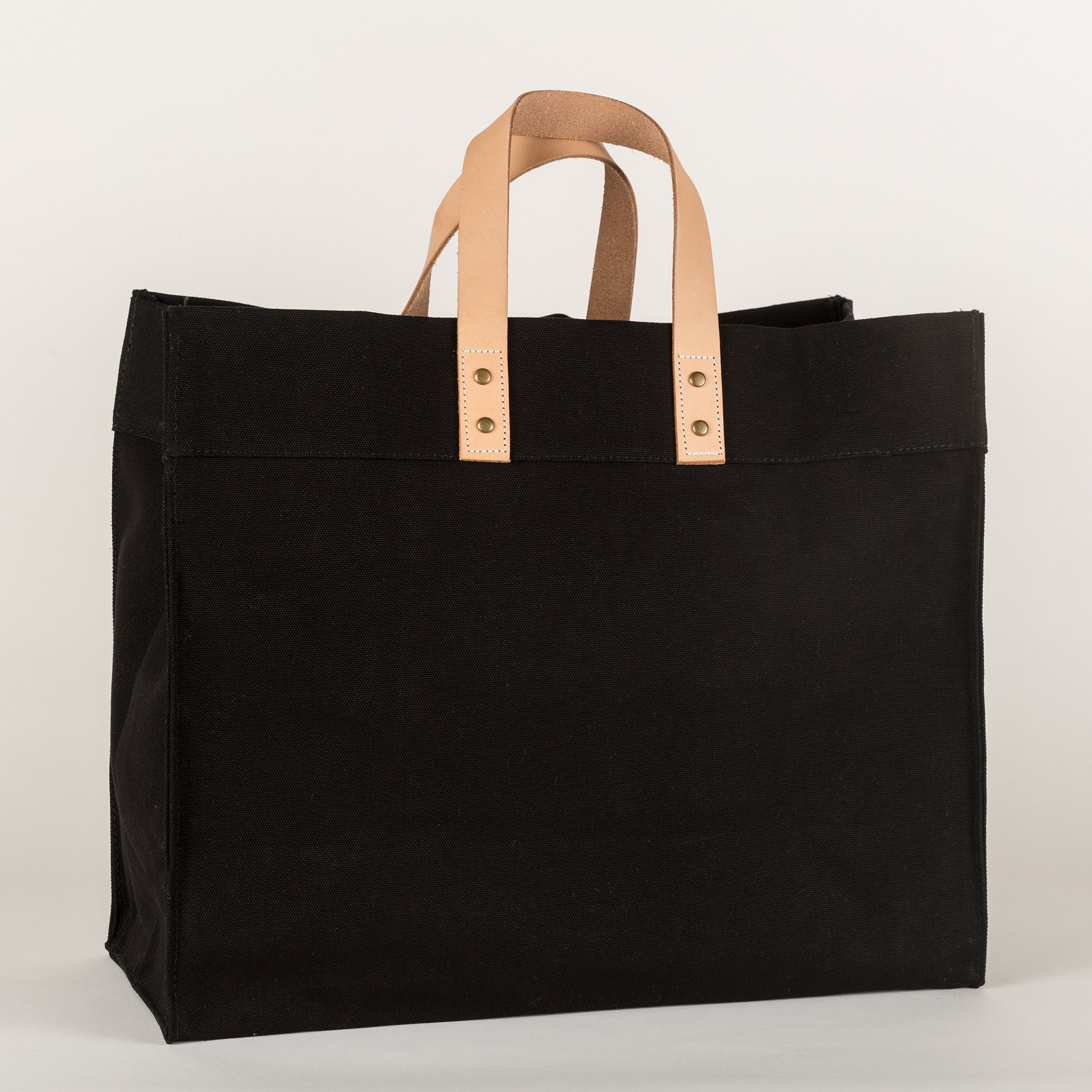 A stylish Box Tote Bag made of heavyweight canvas with thick leather handles and metal studs, perfect for outdoor gatherings.