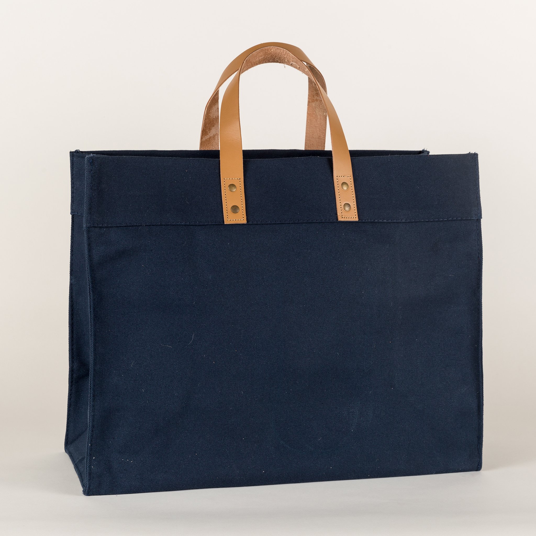 A stylish Box Tote Bag made of heavyweight canvas with thick leather handles and metal studs, perfect for outdoor gatherings.