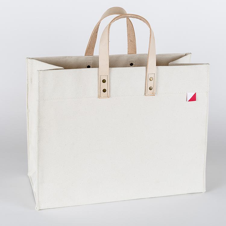 A stylish Box Tote Bag made of heavyweight canvas with thick leather handles and metal studs, perfect for outdoor gatherings.