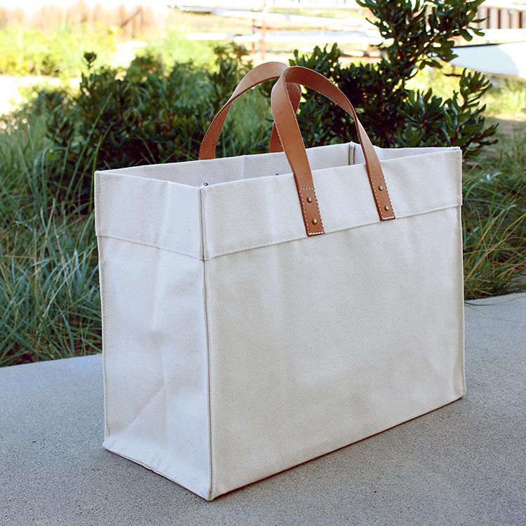 A stylish Box Tote Bag made of heavyweight canvas with thick leather handles and metal studs, perfect for outdoor gatherings.