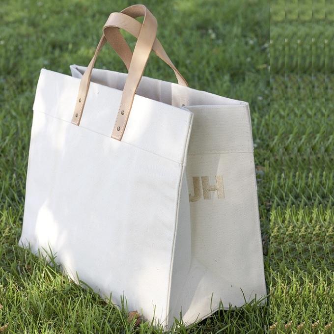 A stylish Box Tote Bag made of heavyweight canvas with thick leather handles and metal studs, perfect for outdoor gatherings.