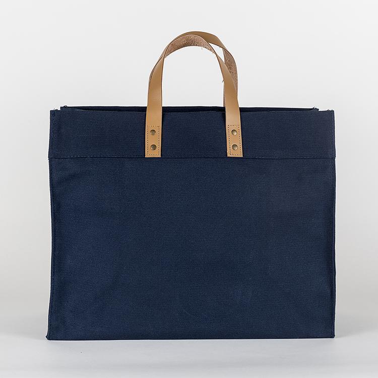 A stylish Box Tote Bag made of heavyweight canvas with thick leather handles and metal studs, perfect for outdoor gatherings.