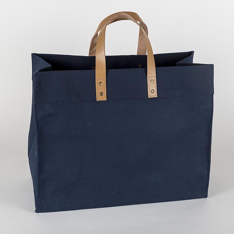 A stylish Box Tote Bag made of heavyweight canvas with thick leather handles and metal studs, perfect for outdoor gatherings.