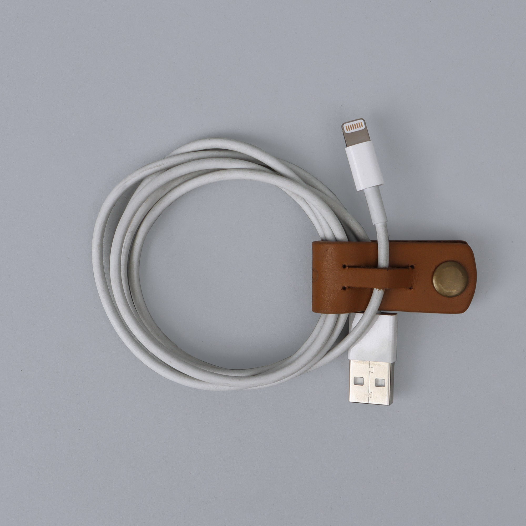 A stylish and minimalistic cable wrap made from durable harness leather, featuring brass rivets and a refined finish.