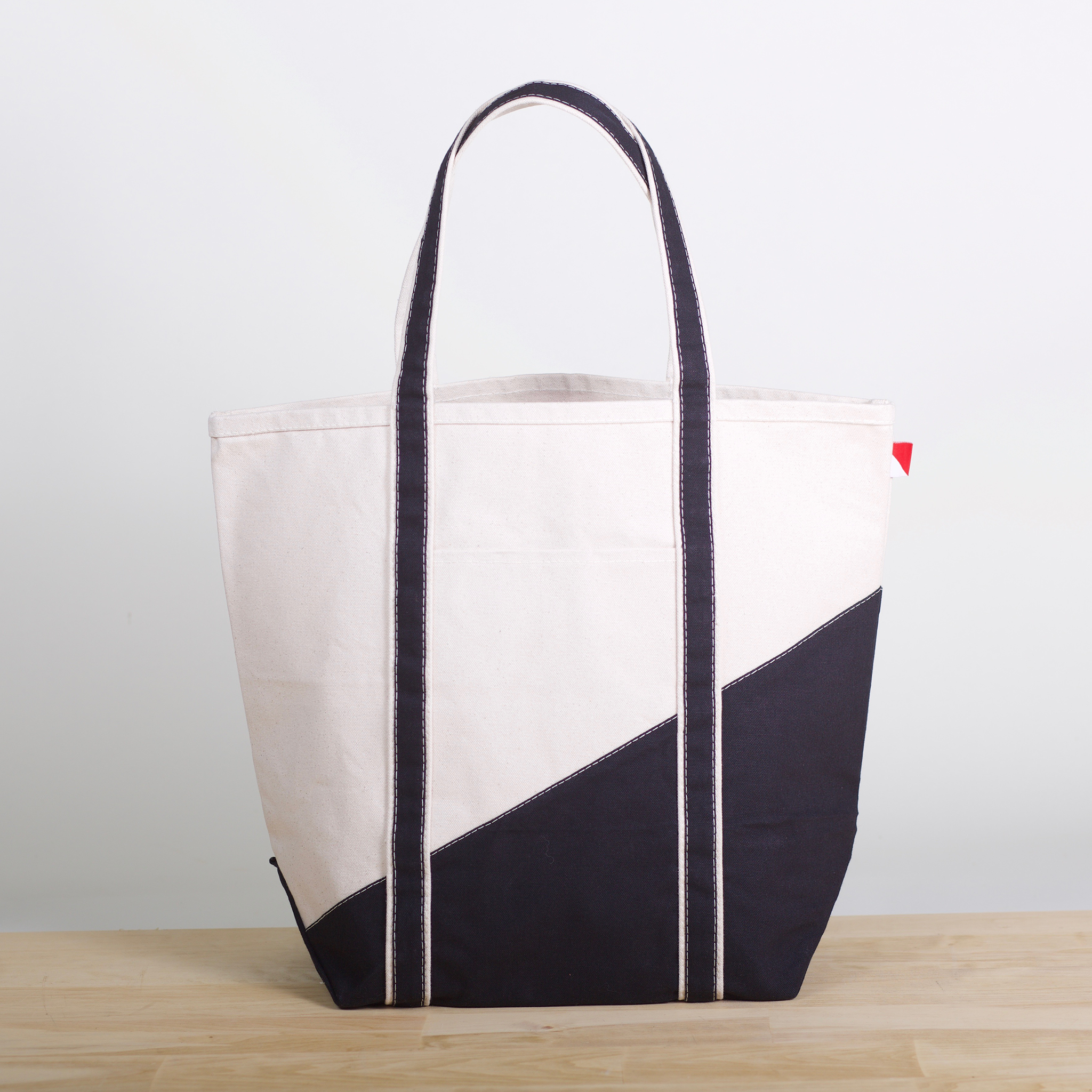 A large contemporary tote bag featuring a diagonal sail design, reinforced handles, and multiple interior pockets for organization.