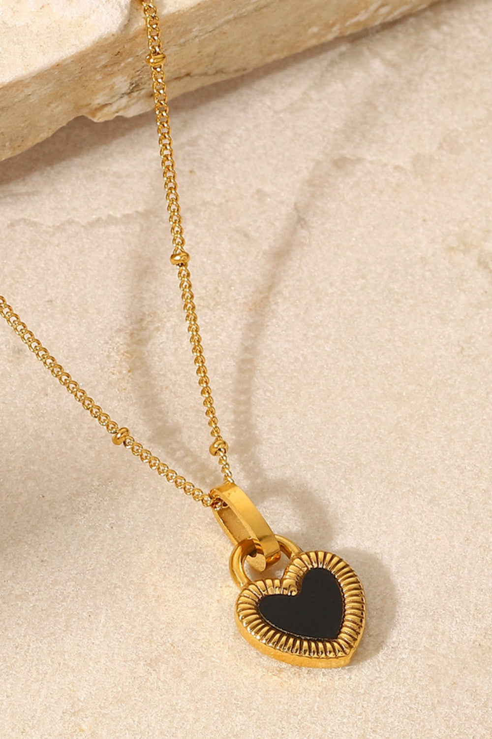 A stylish Contrast Heart Pendant Necklace featuring a heart-shaped pendant on a stainless steel chain, elegantly displayed in a flat lay style.