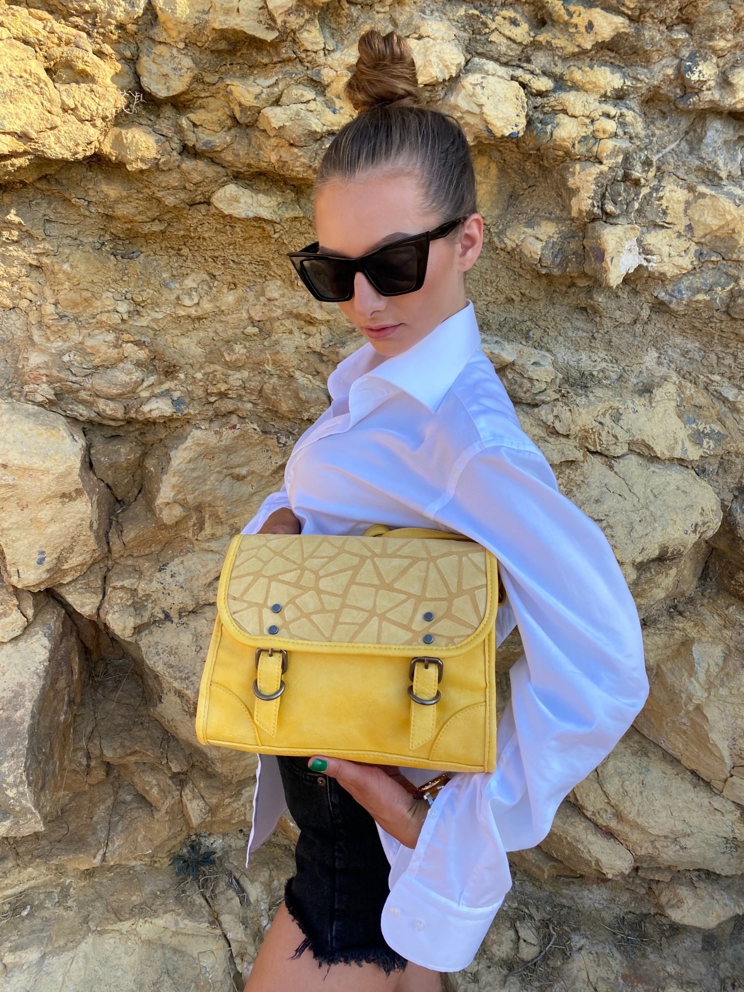 Stylish yellow crossbody bag with buckle and adjustable strap, featuring metallic details and a lined interior.