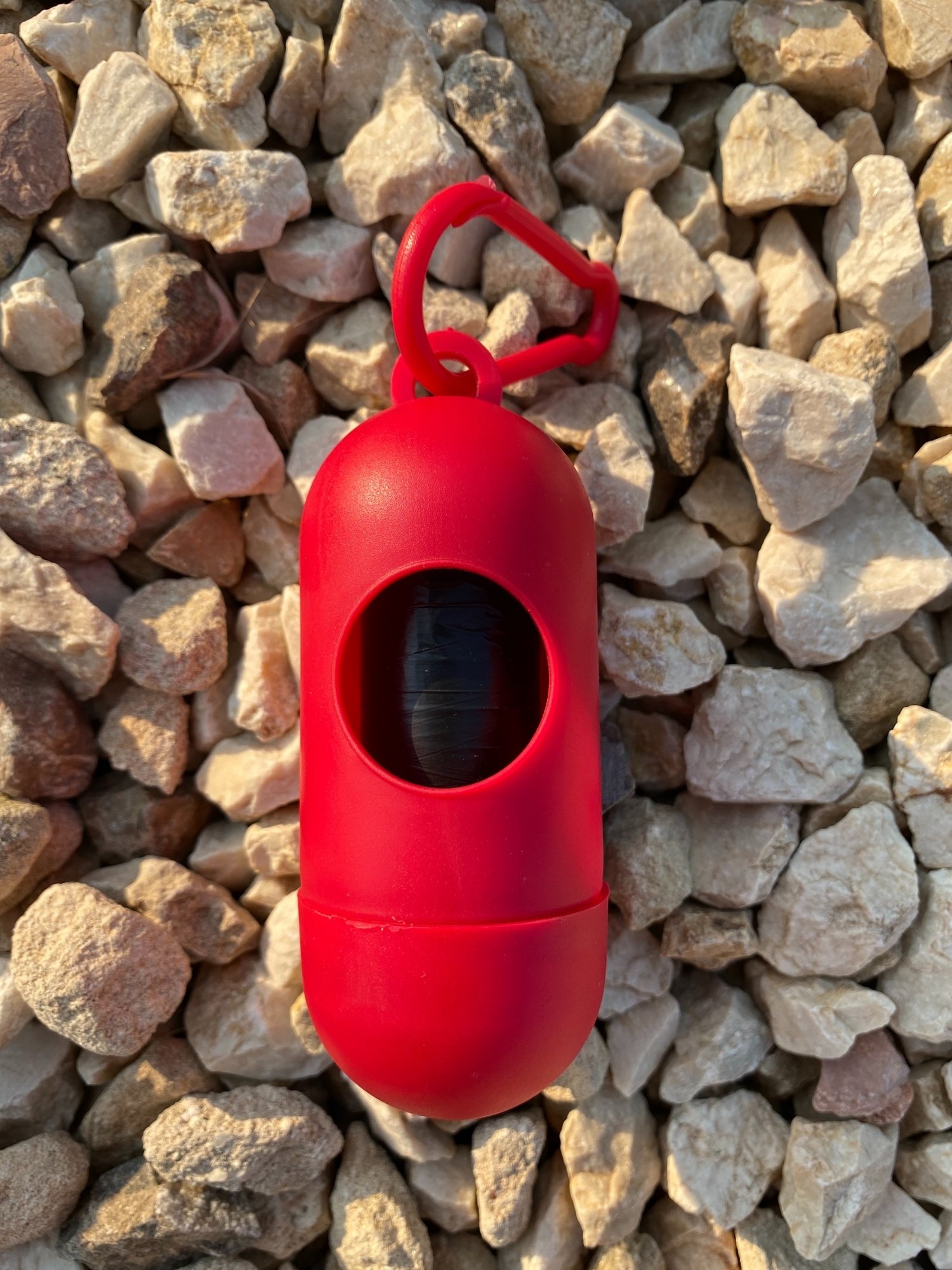 Dog Poop Bag Dispenser in Blue, Red, and Green colors with bags attached, showcasing its carabiner clip and easy-access slot.