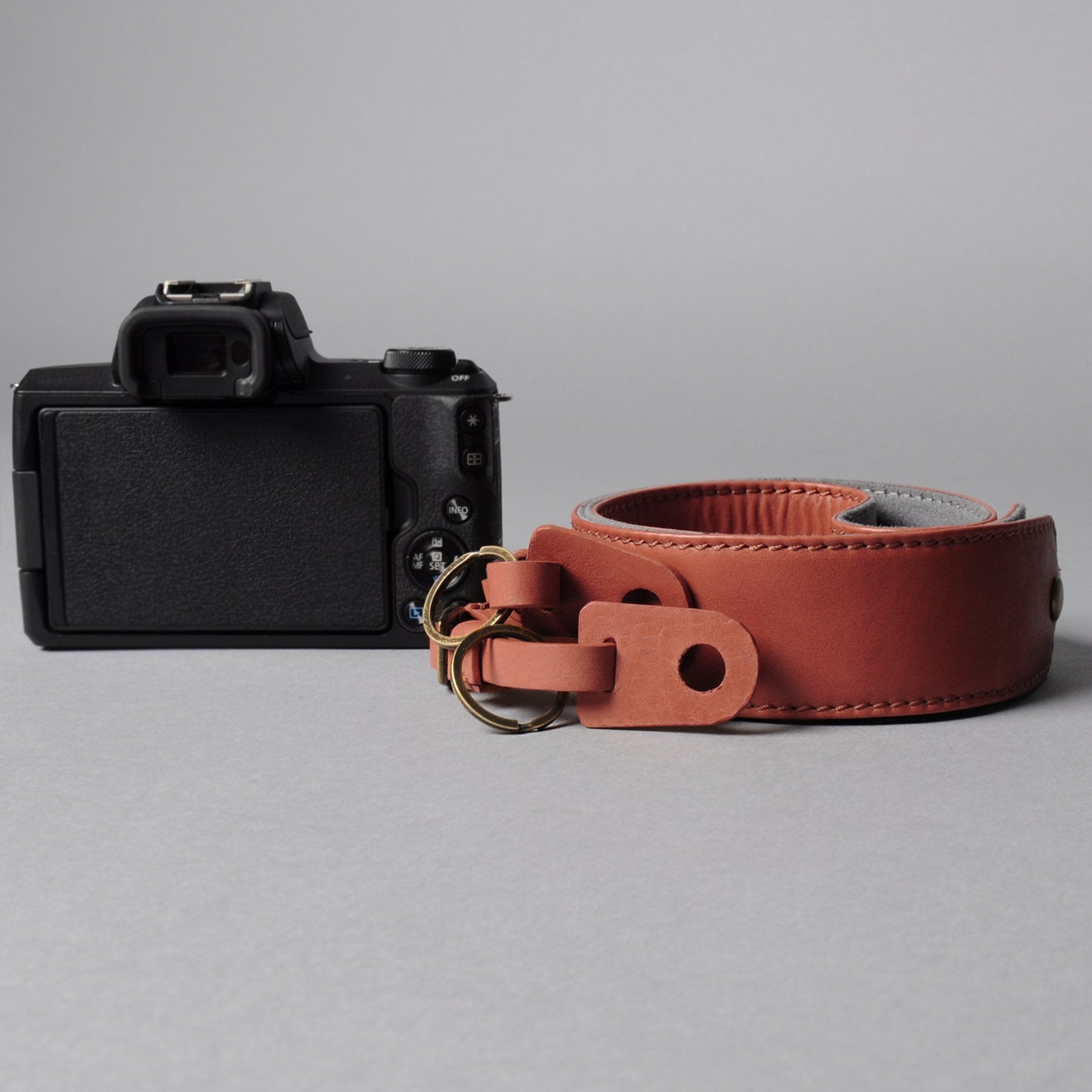 A stylish DSLR camera leather strap made from durable harness leather with antique brass hardware, showcasing its adjustable length and metal rings.