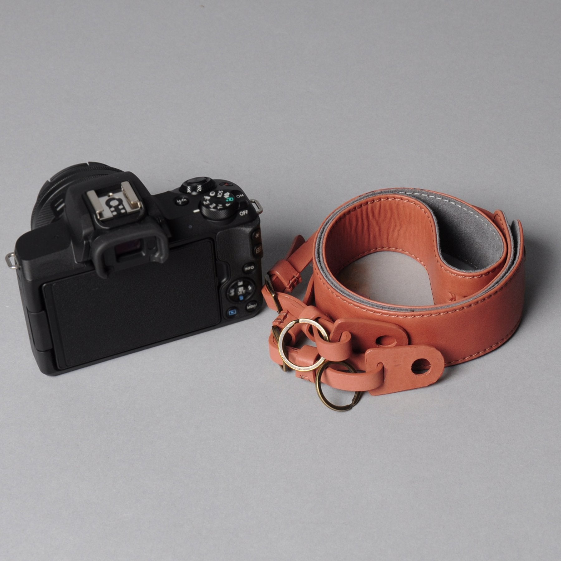 A stylish DSLR camera leather strap made from durable harness leather with antique brass hardware, showcasing its adjustable length and metal rings.