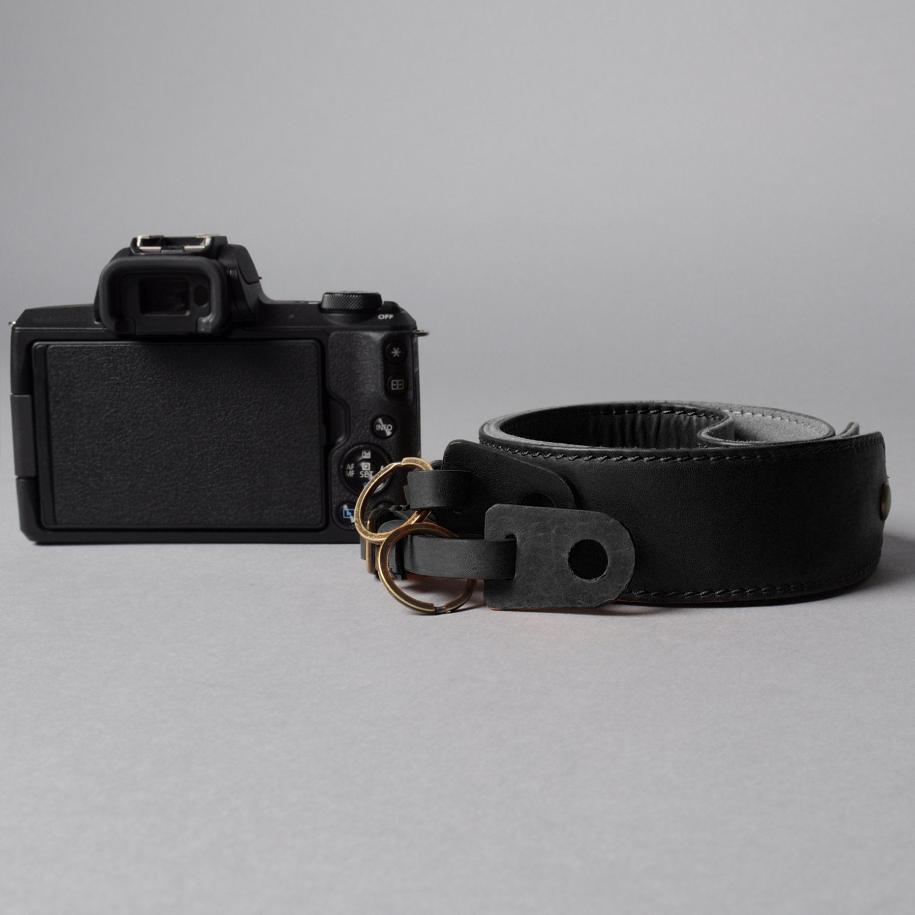 A stylish DSLR camera leather strap made from durable harness leather with antique brass hardware, showcasing its adjustable length and metal rings.