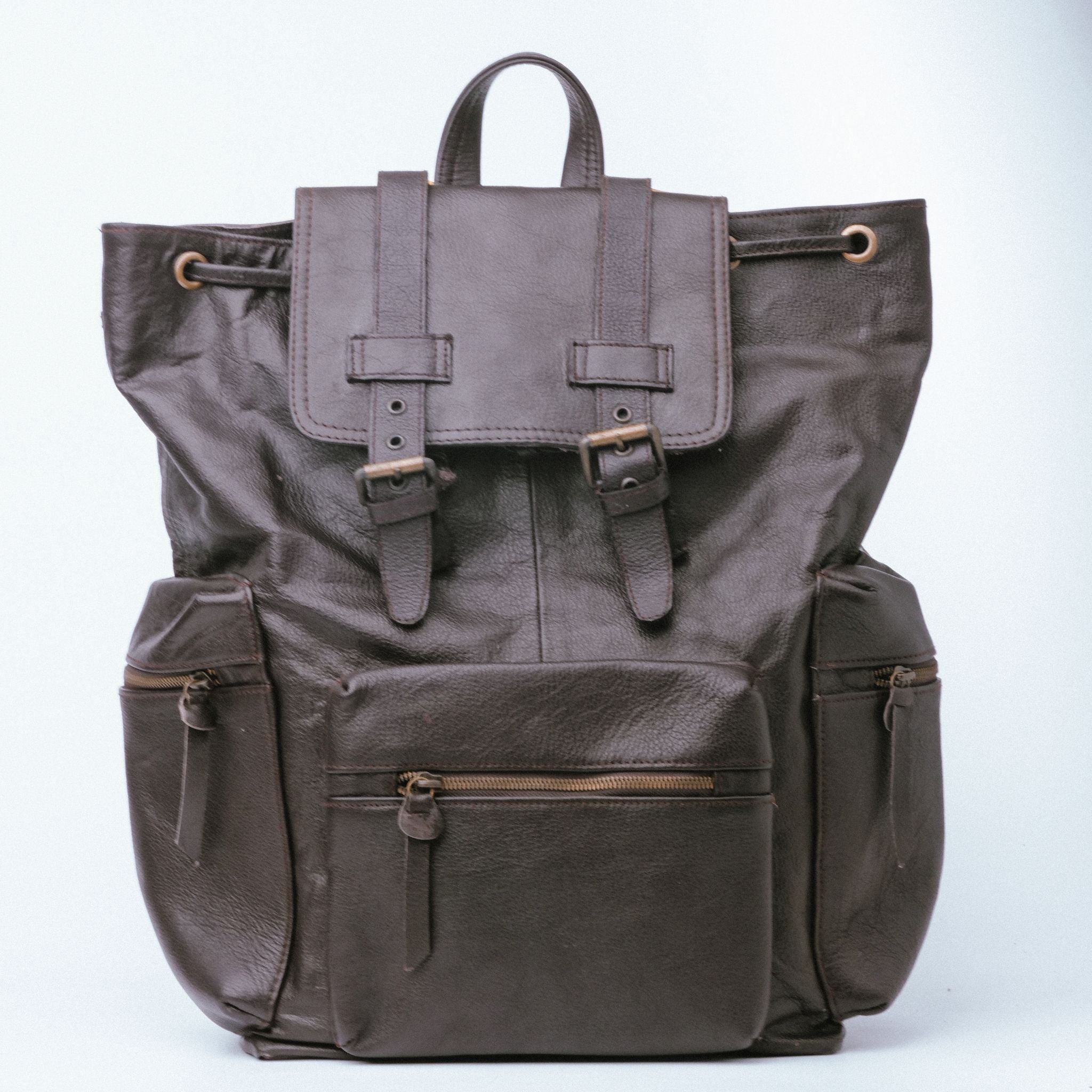 Brown leather backpack with double adjustable straps and golden hardware, featuring side zipper pockets and a top handle.