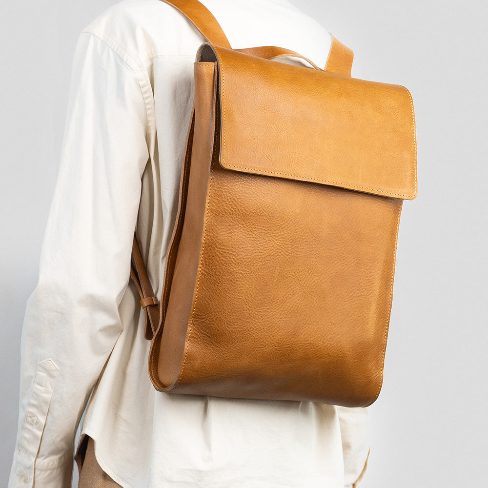 Tan leather laptop backpack with adjustable straps and multiple pockets, showcasing its minimalist design and eco-friendly materials.