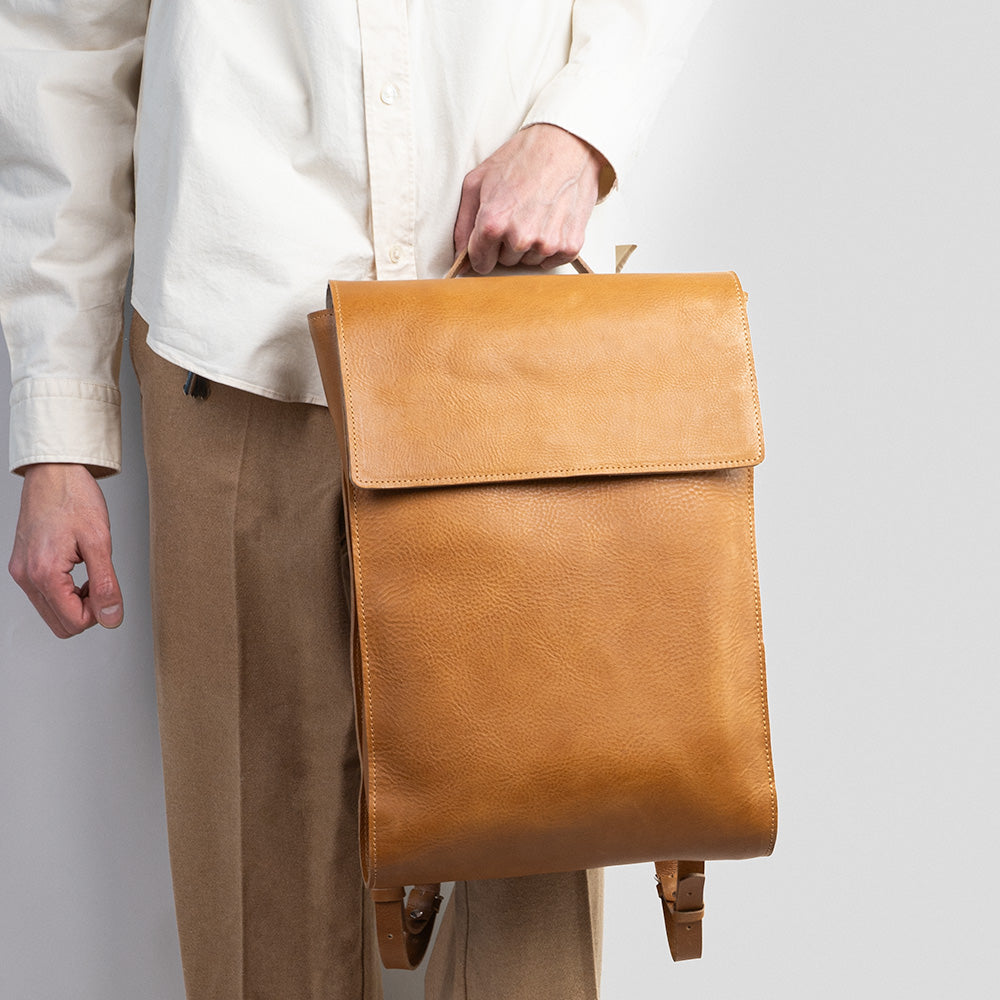 Tan leather laptop backpack with adjustable straps and multiple pockets, showcasing its minimalist design and eco-friendly materials.