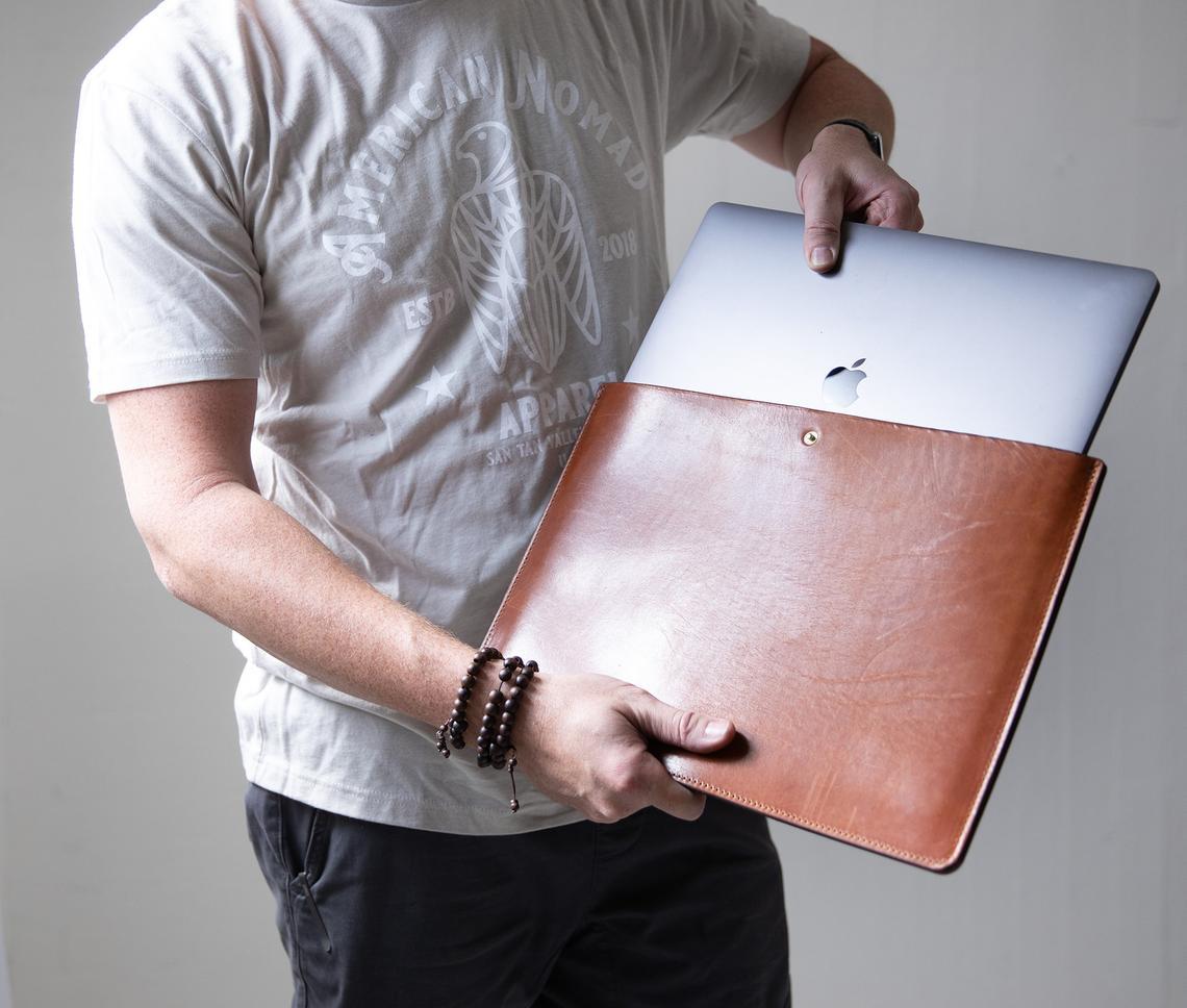 Personalized leather laptop sleeve made from genuine full grain leather, featuring a secure strap and brass snap, ideal for 13"-15" laptops.