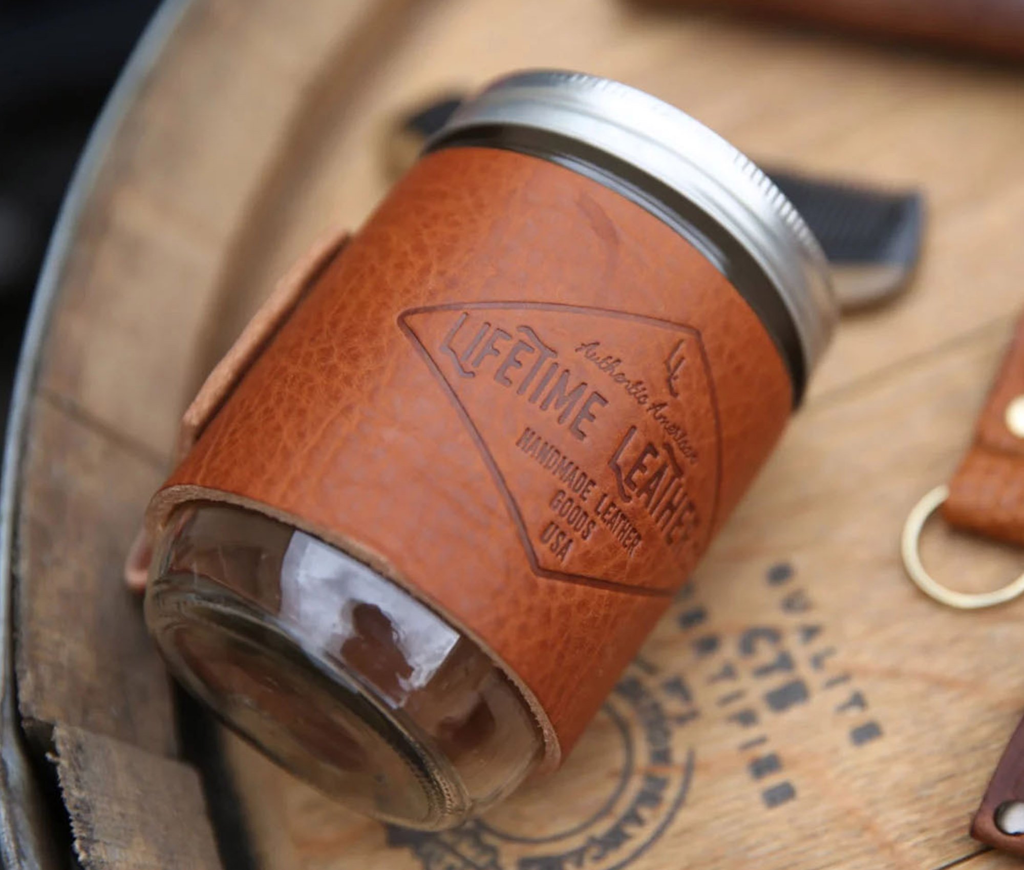 Leather Mason Jar Coozie hugging a Mason jar, showcasing its hand-stitched design and riveted handle.