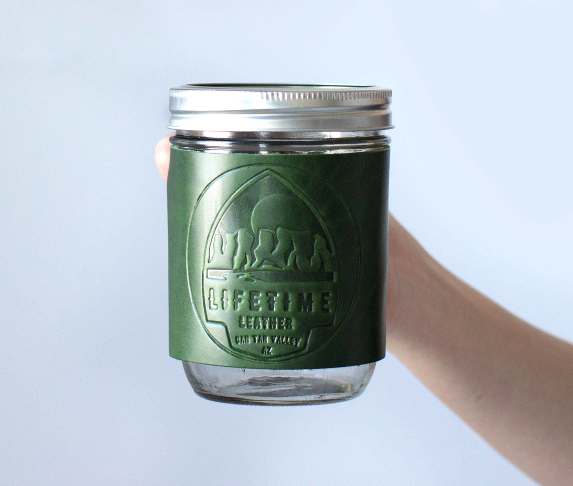 Leather Mason Jar Coozie hugging a Mason jar, showcasing its hand-stitched design and riveted handle.