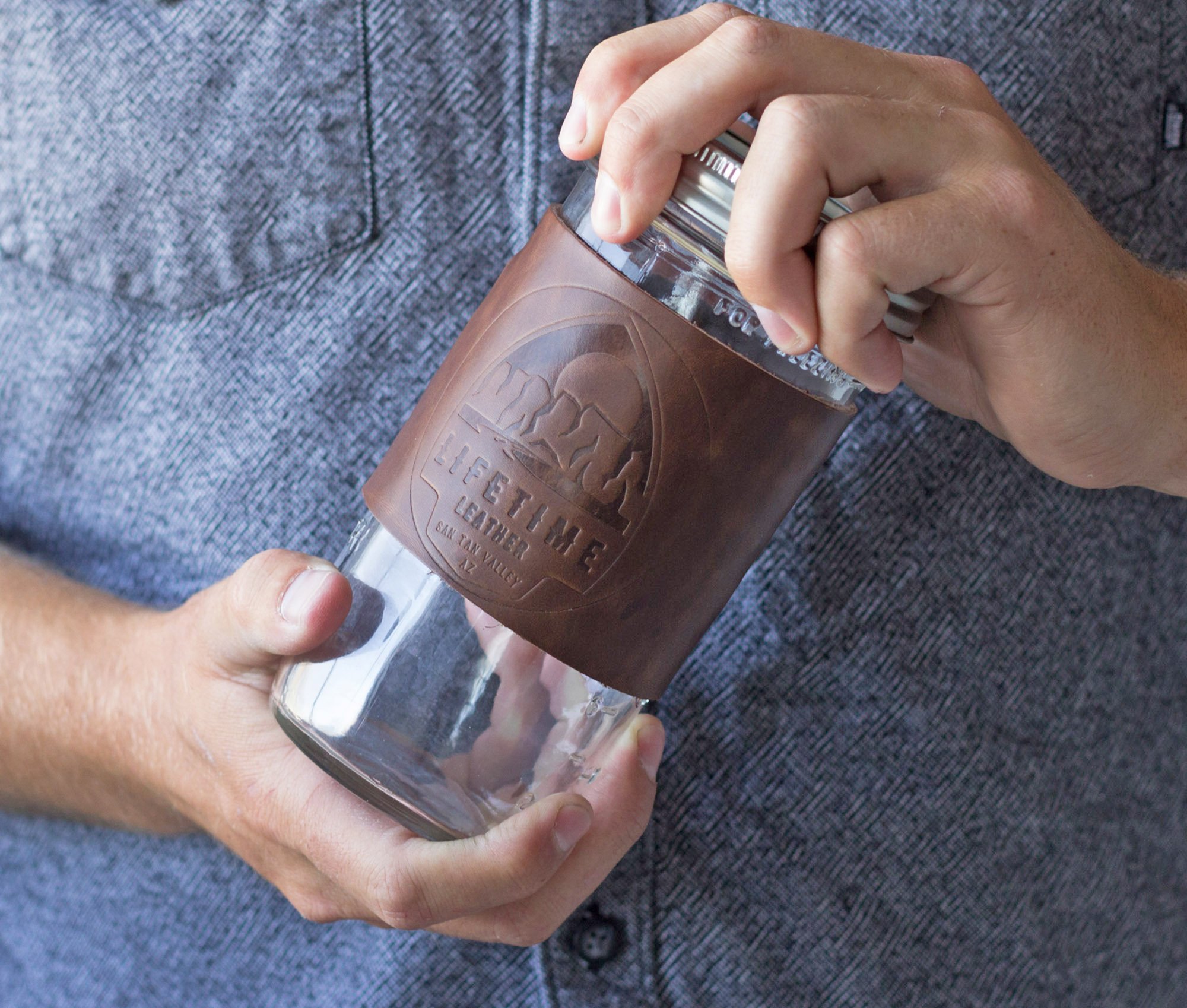 Leather Mason Jar Coozie hugging a Mason jar, showcasing its hand-stitched design and riveted handle.