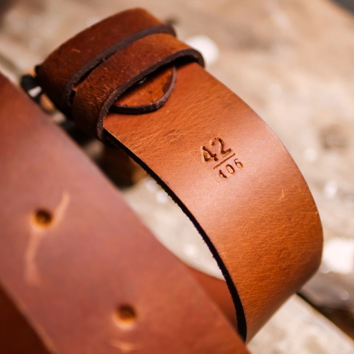 A rustic leather belt with double thread stitching and a single pin buckle, showcasing its quality and style.