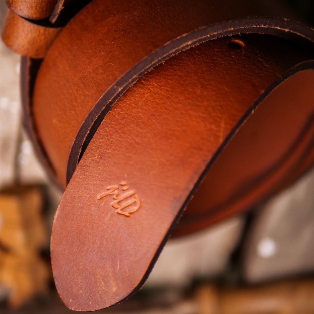 A rustic leather belt with double thread stitching and a single pin buckle, showcasing its quality and style.