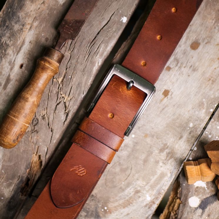 A rustic leather belt with double thread stitching and a single pin buckle, showcasing its quality and style.