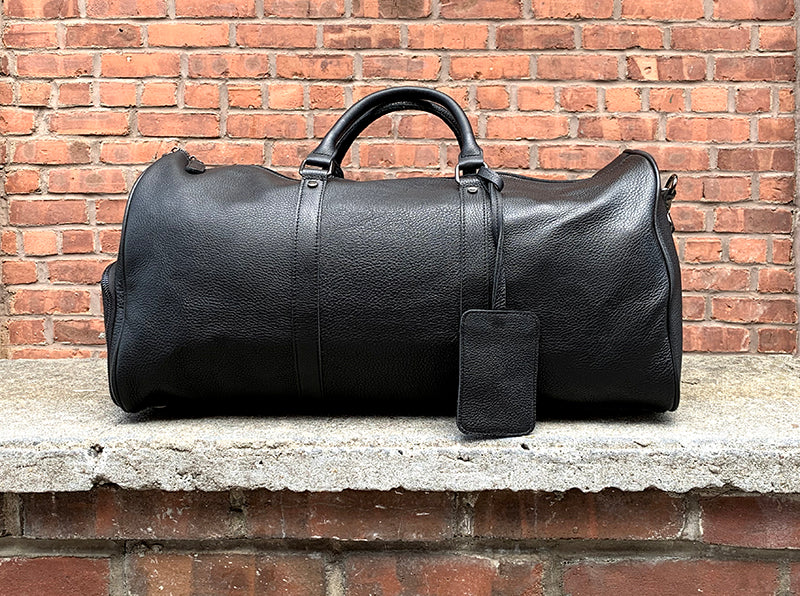 The Endre Weekender vintage leather duffle bag in black, showcasing its smooth texture and stylish design with leather handles and shoulder strap.